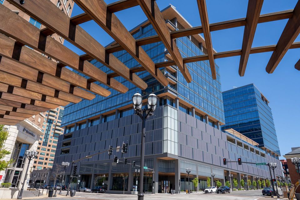 Modern glass and steel buildings under a wooden pergola on a sunny day.
