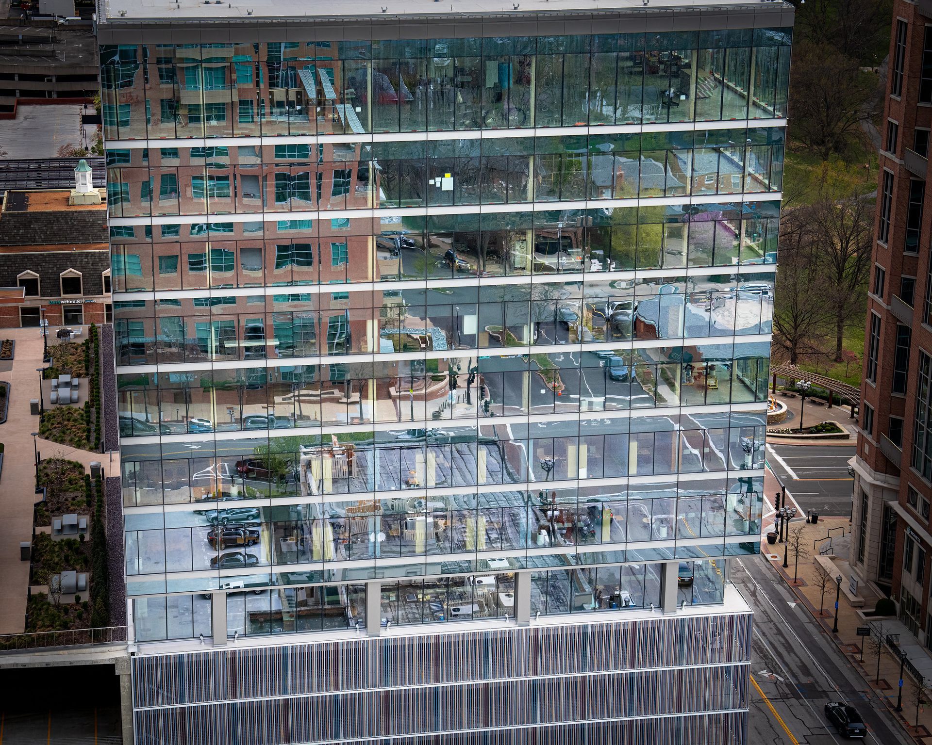 Modern glass skyscraper reflects surrounding buildings and sky.