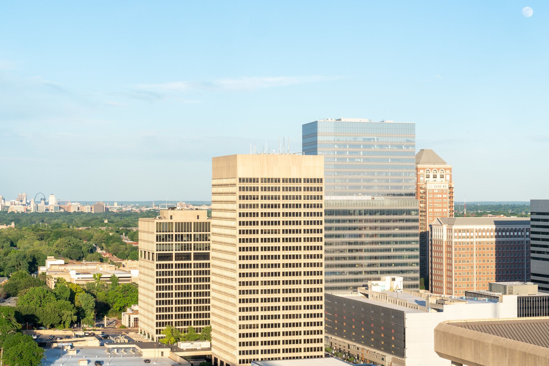 City skyline with beige, glass, and brick high-rise buildings under a pale blue sky.