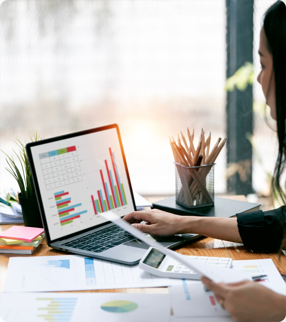 Woman at desk with laptop displaying financial charts, calculator, papers, and pencils.