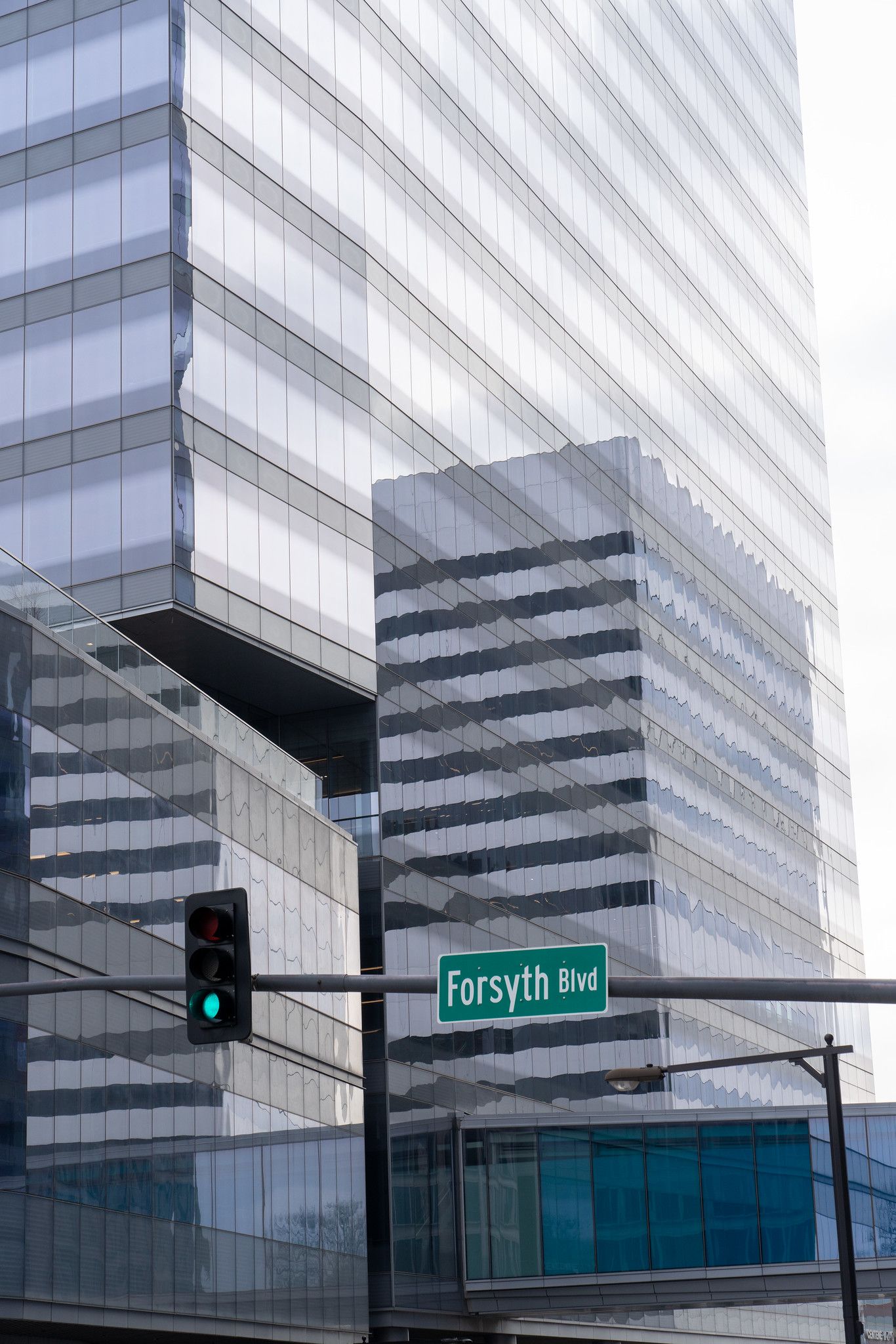 Modern glass skyscraper with green traffic light and street sign 