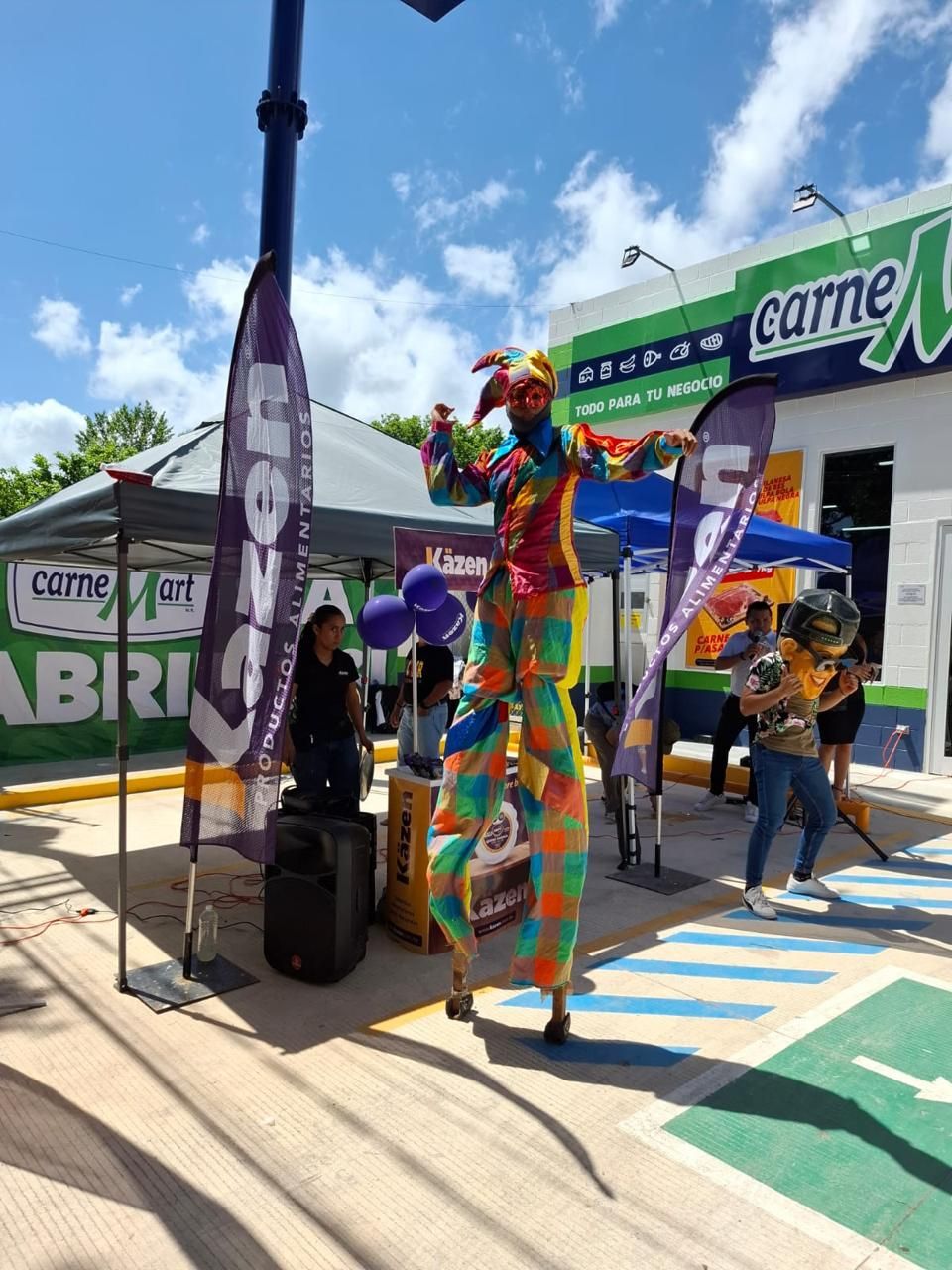 Payaso en zancos en la inauguración de un negocio, vistiendo ropa colorida.