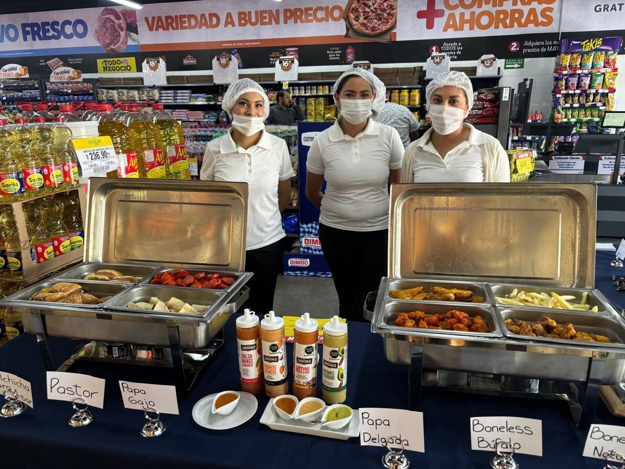 Tres mujeres con máscaras y sombreros permanecen detrás de calentadores de alimentos en un supermercado.