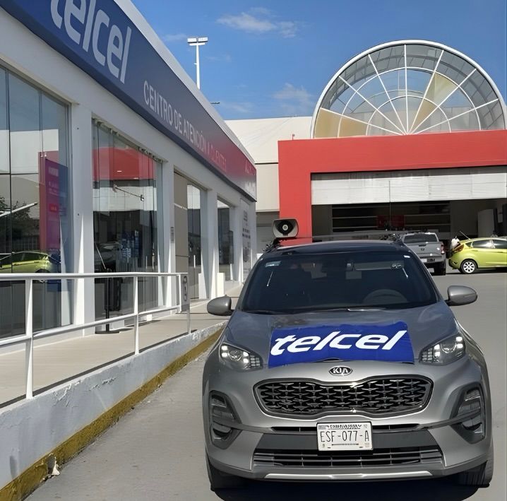 Kia Sportage color gris con logo Telcel frente a una tienda Telcel.