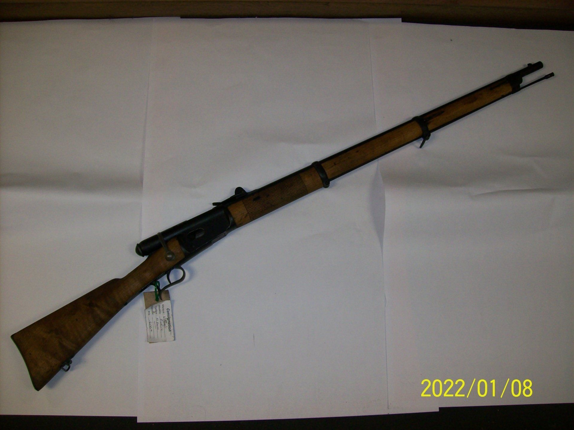 Fusil en bois avec canon et garnitures en métal, posé sur une surface blanche.