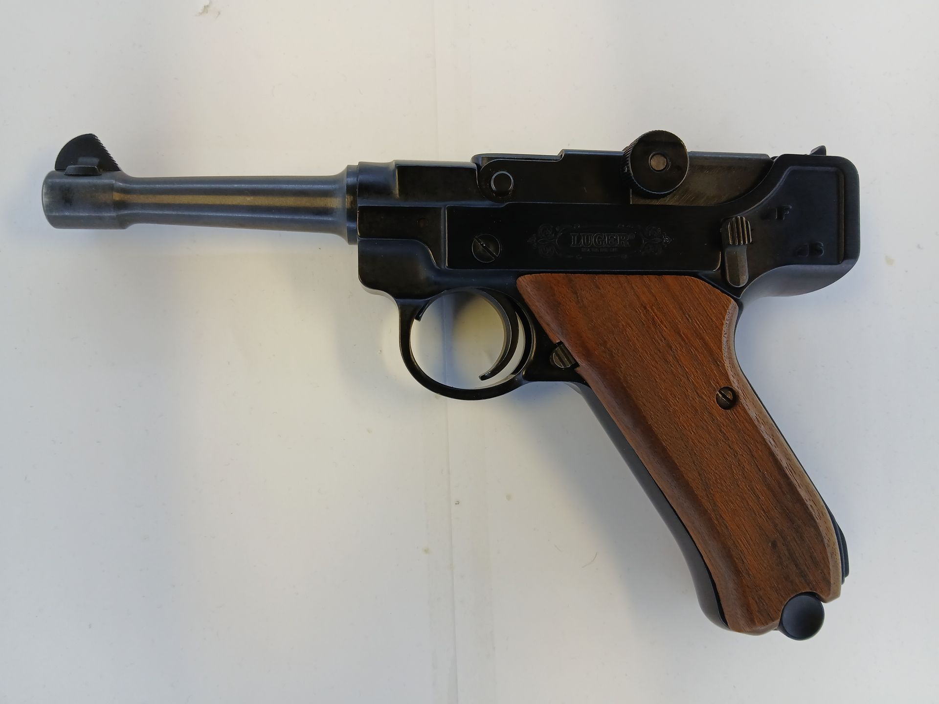 Black and brown handgun with a wooden grip, resting on a white surface.