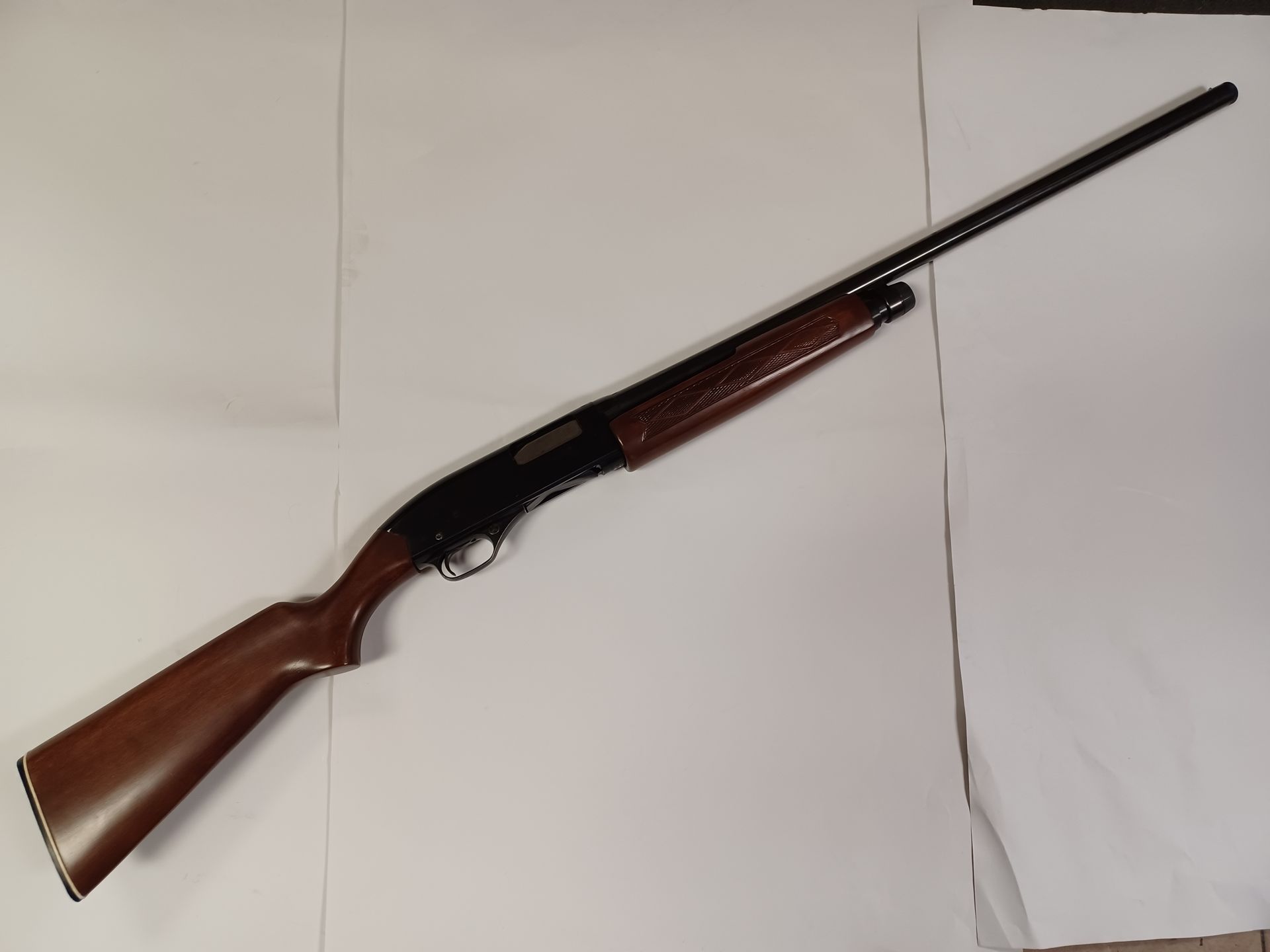 Un fusil de chasse marron et noir posé en diagonale sur une surface blanche.