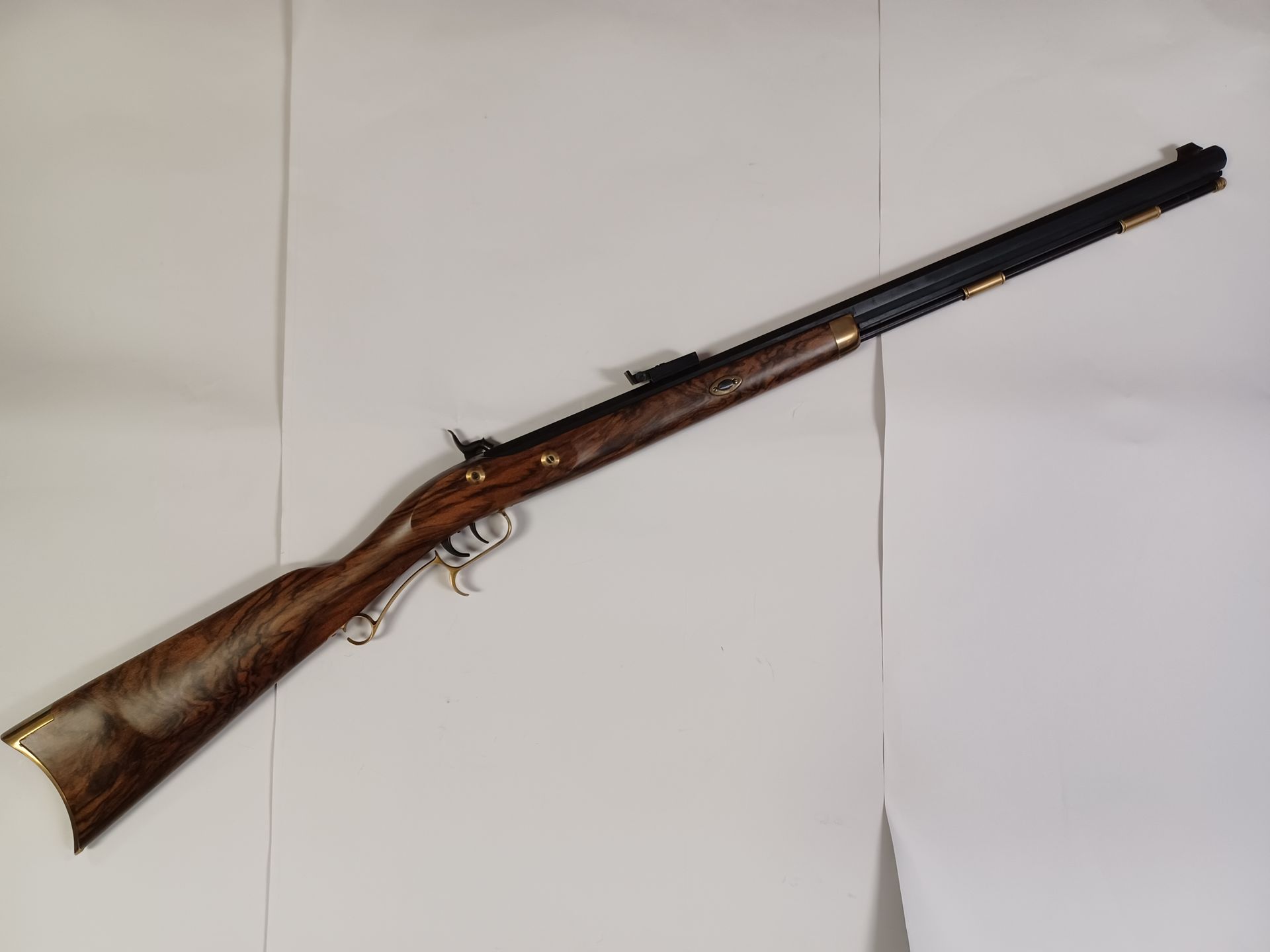 Fusil antique marron et noir avec crosse en bois et accents métalliques, incliné sur fond blanc.