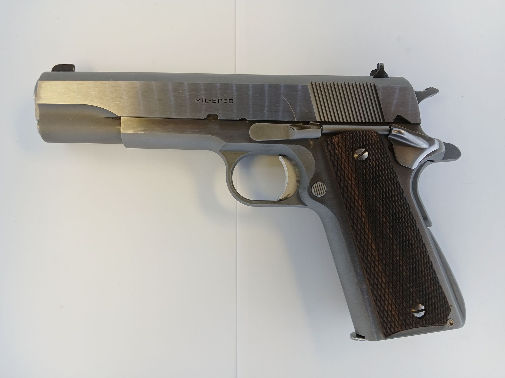 Stainless steel semi-automatic pistol with wooden grips, resting on a white surface.