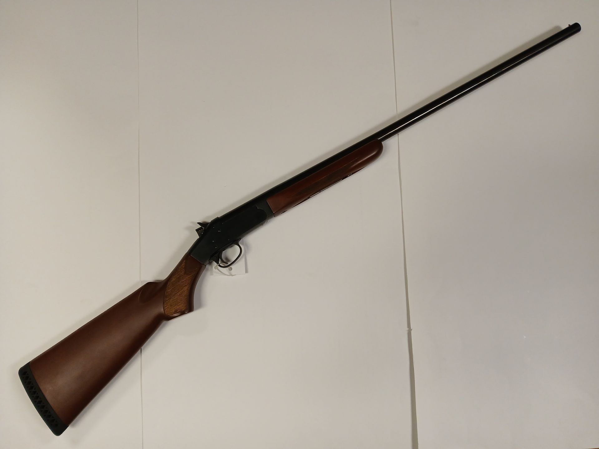 Fusil de chasse à un coup avec une crosse en bois et un long canon noir, incliné sur un fond blanc.