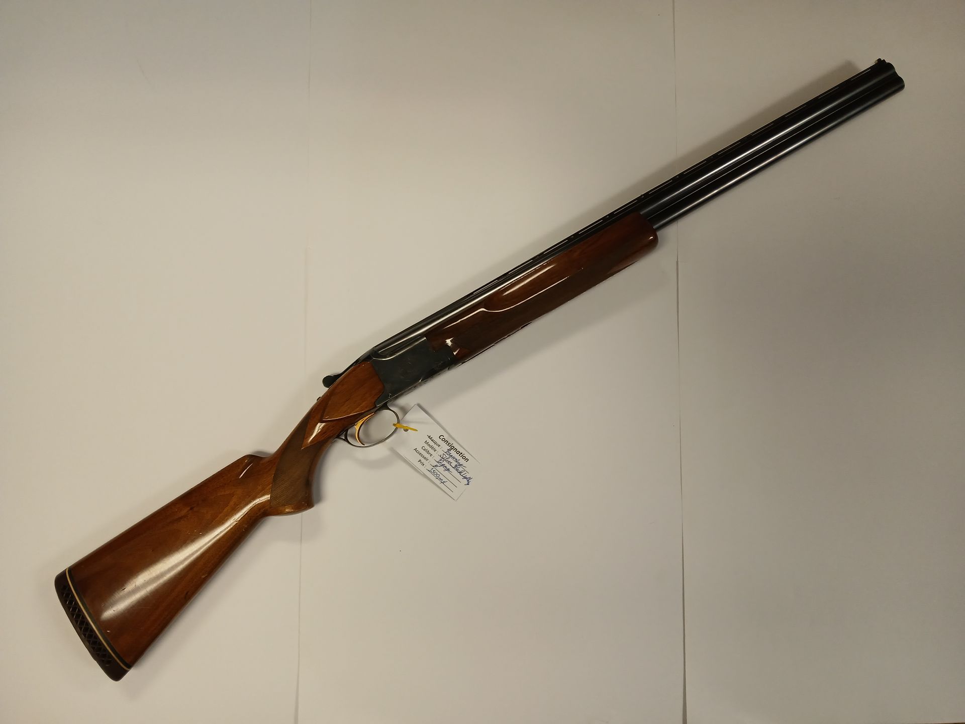 Fusil superposé marron et noir avec crosse en bois, posé sur un fond blanc.