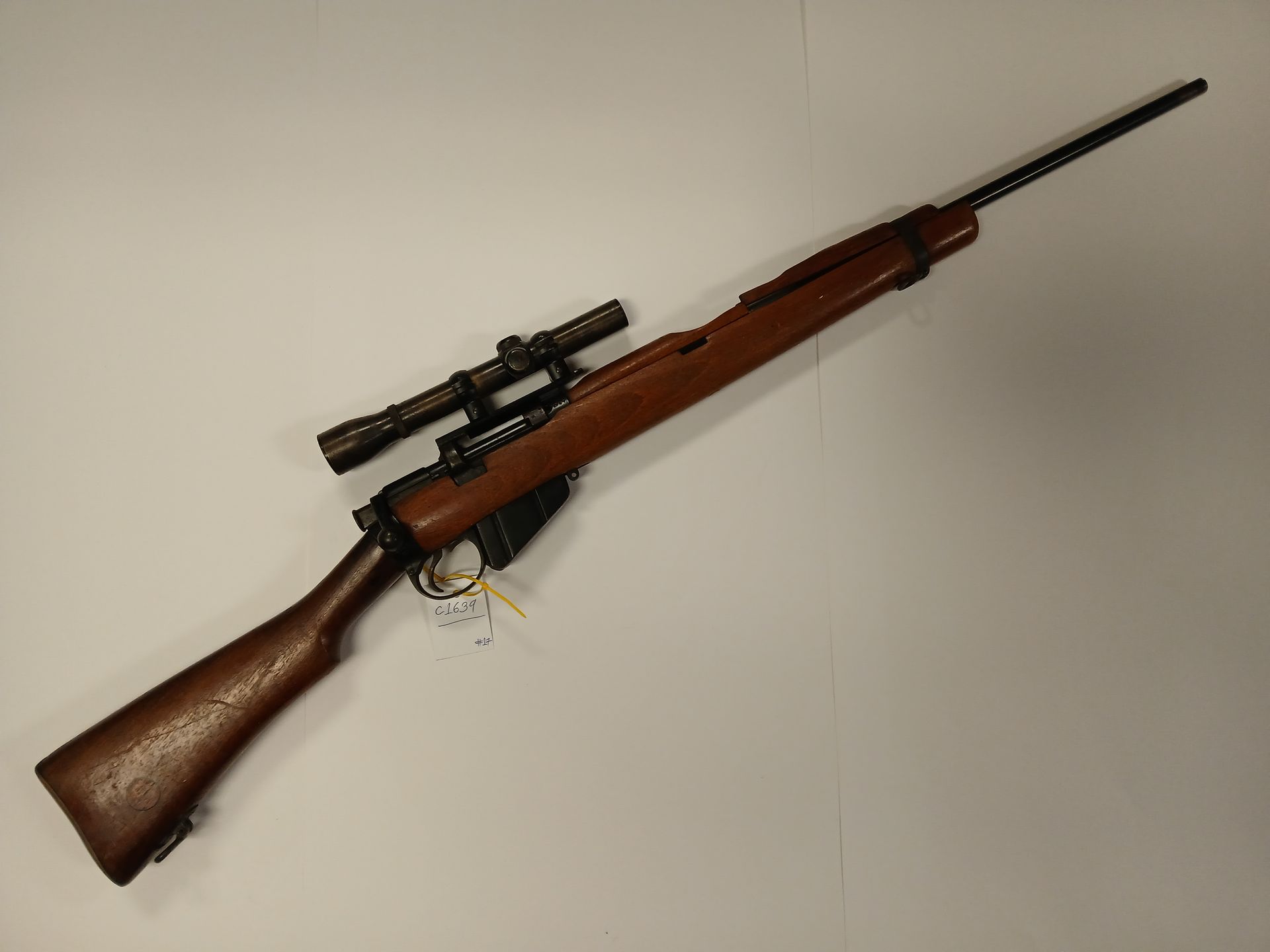 Un fusil à crosse en bois avec une lunette, posé sur une surface blanche.