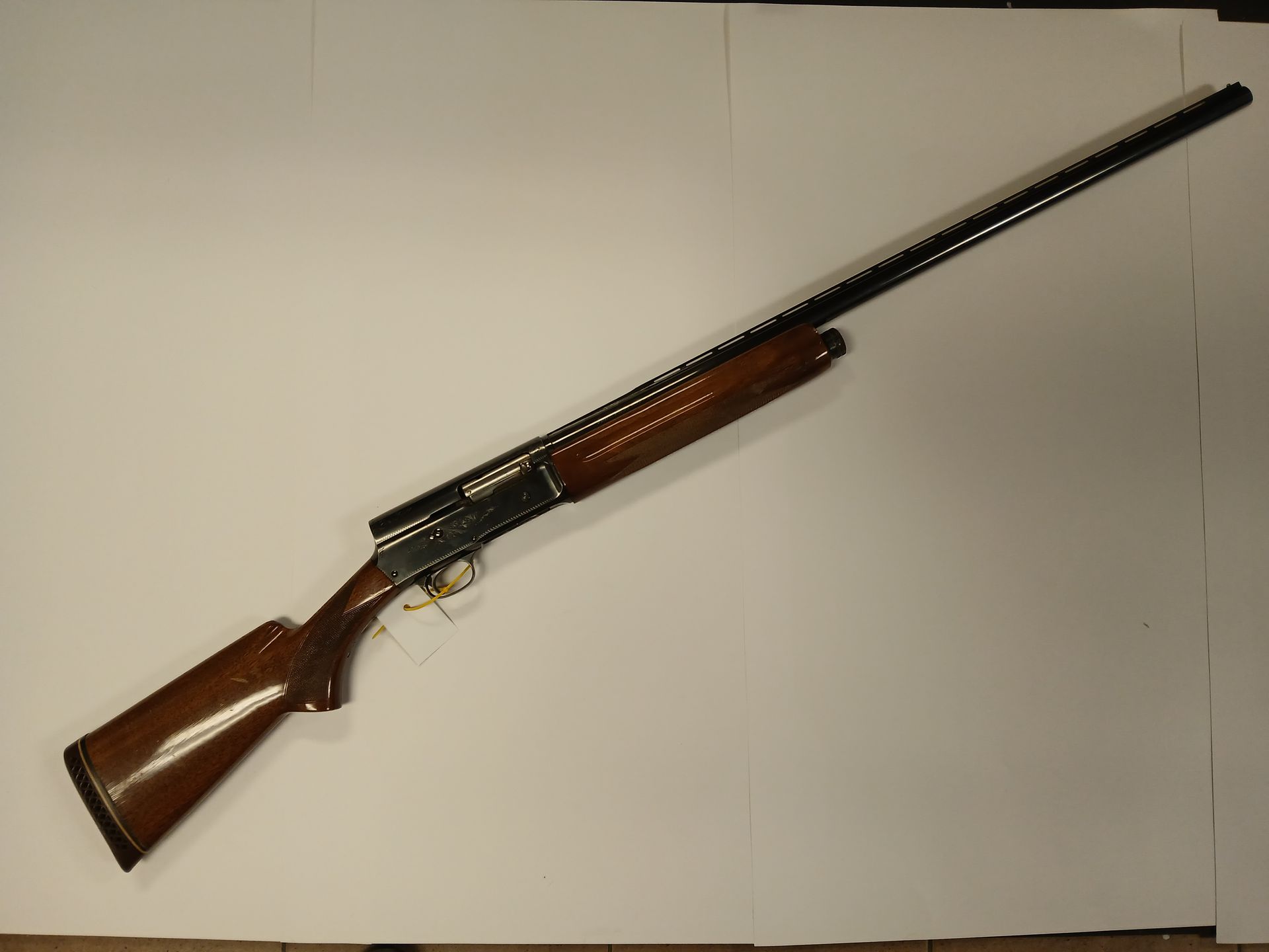 Fusil de chasse marron et noir avec une crosse en bois et un long canon, posé sur une surface blanche.