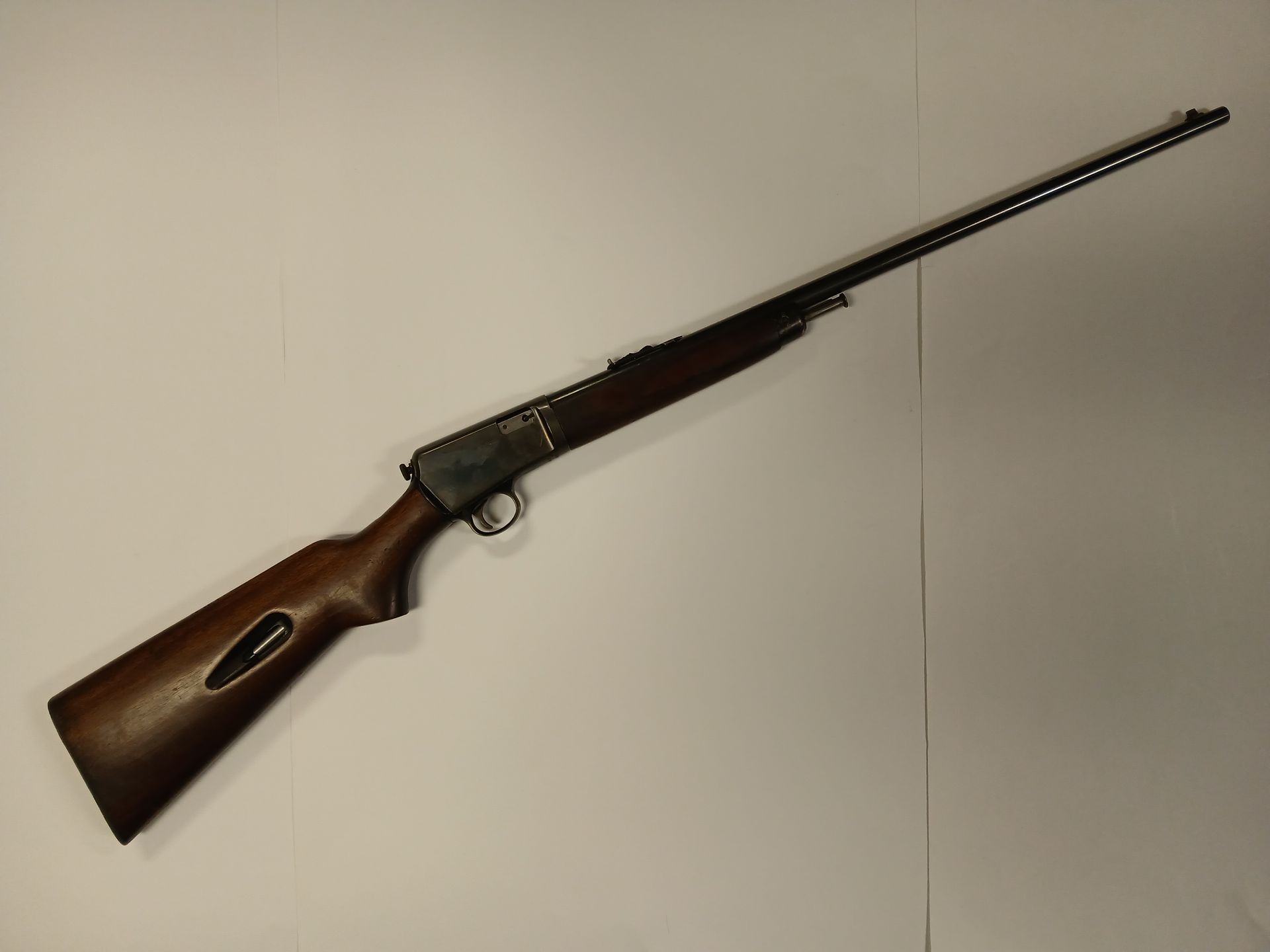 Un fusil à levier vintage avec une crosse en bois, posé sur une surface blanche.
