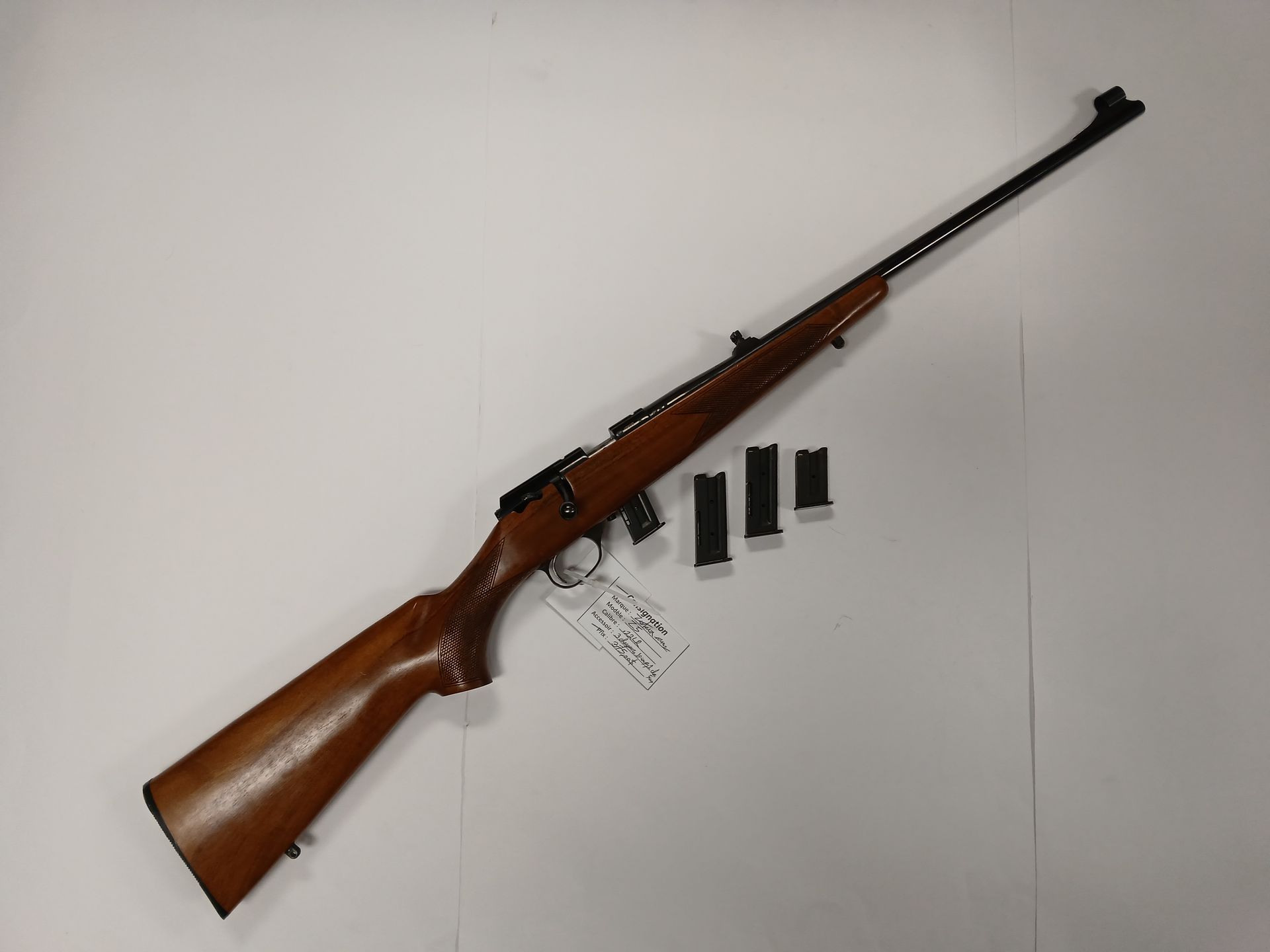 Fusil marron avec canon noir et quatre chargeurs sur une surface blanche.