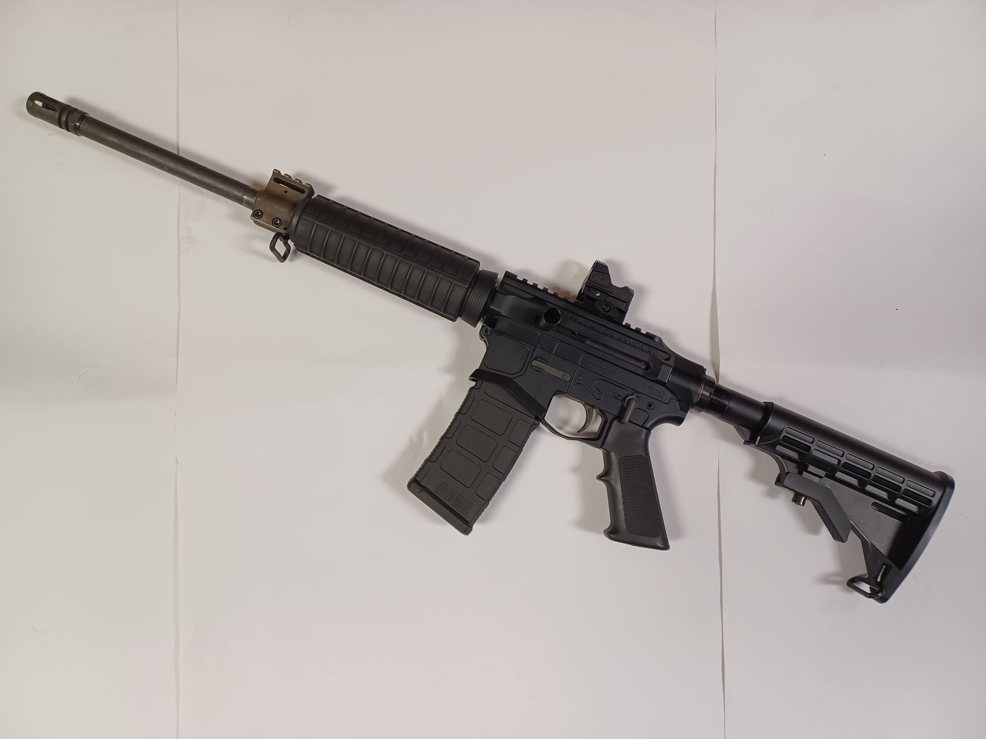 Black AR-15 rifle with attached magazine, mounted scope, and angled foregrip on a white surface.