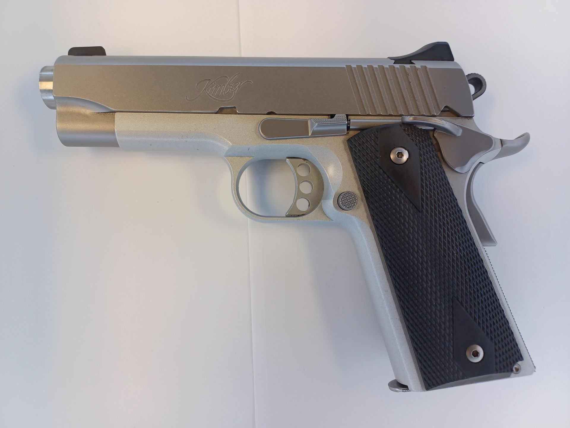 Silver and black handgun, a 1911-style pistol, on a white surface.