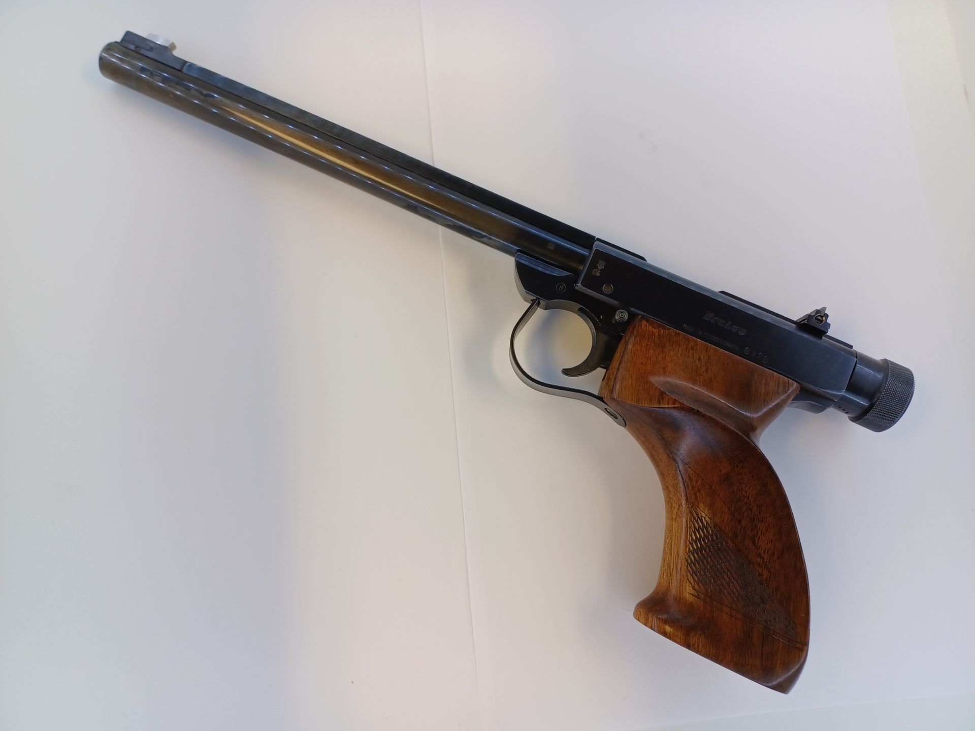Air pistol with wooden grip and black barrel, on a white surface.