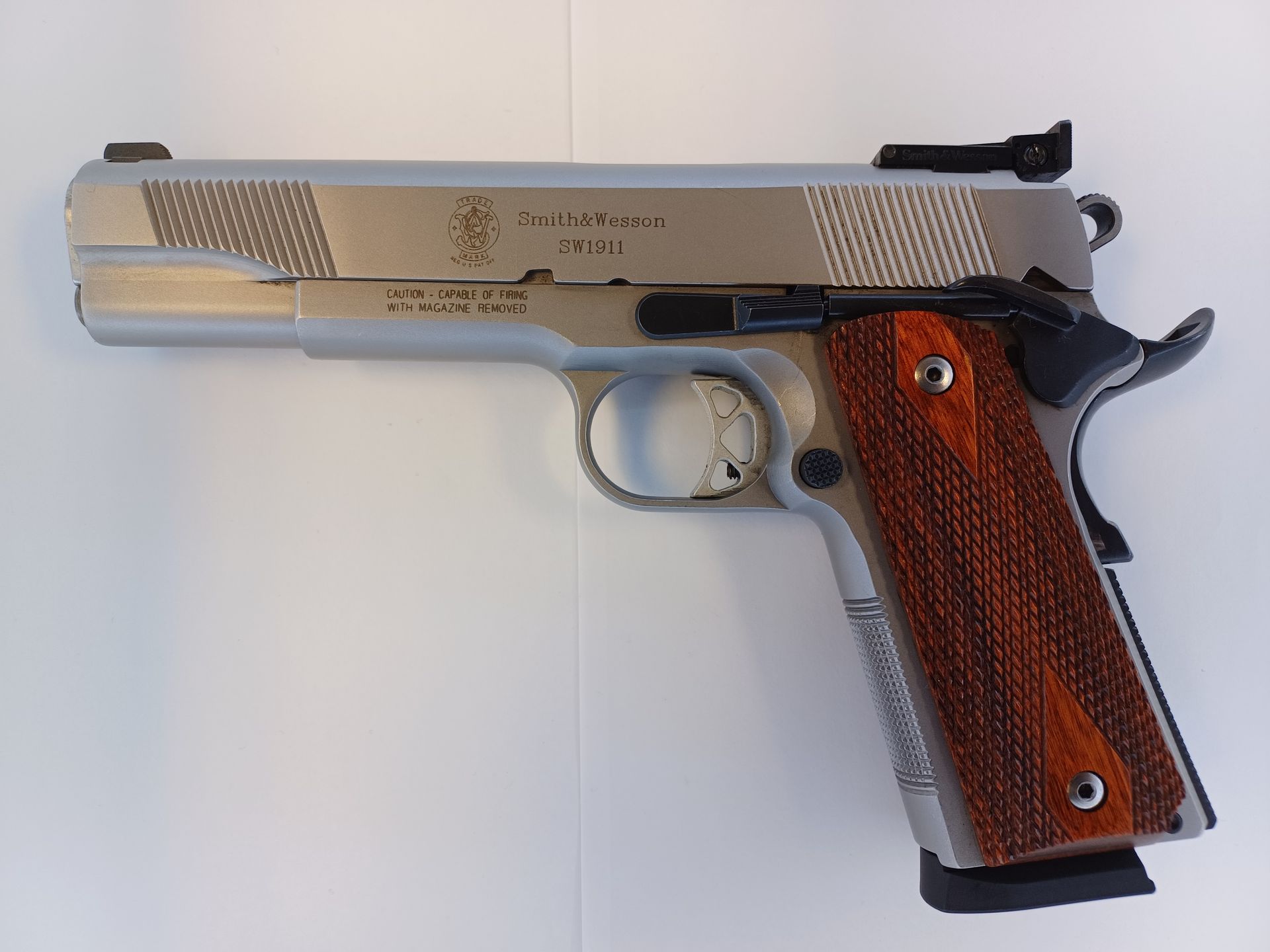 Silver Smith & Wesson 1911 handgun with wooden grips, resting on a white surface.