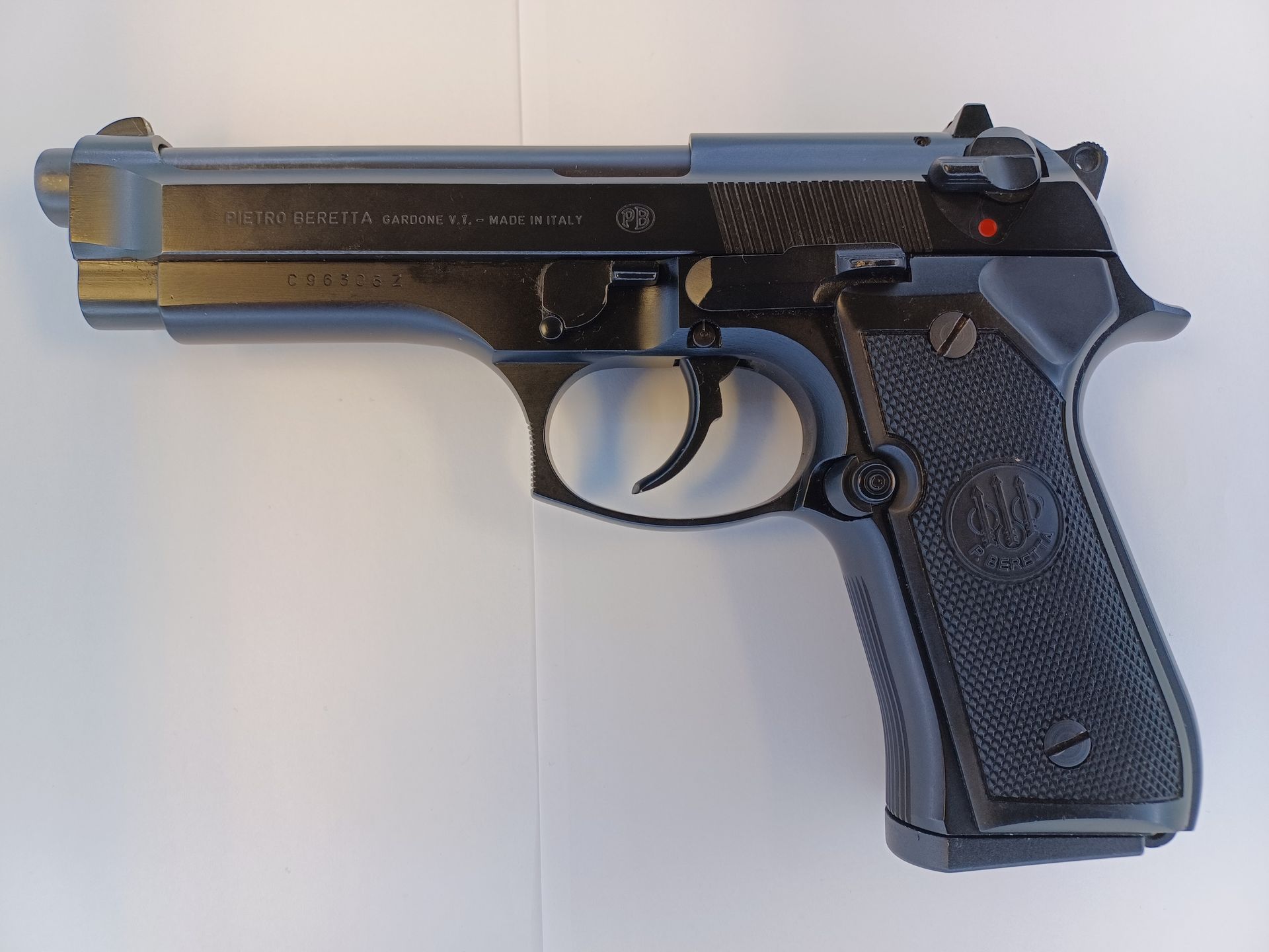 Black Beretta 92FS pistol on a white surface, showing the barrel, trigger, and grip.