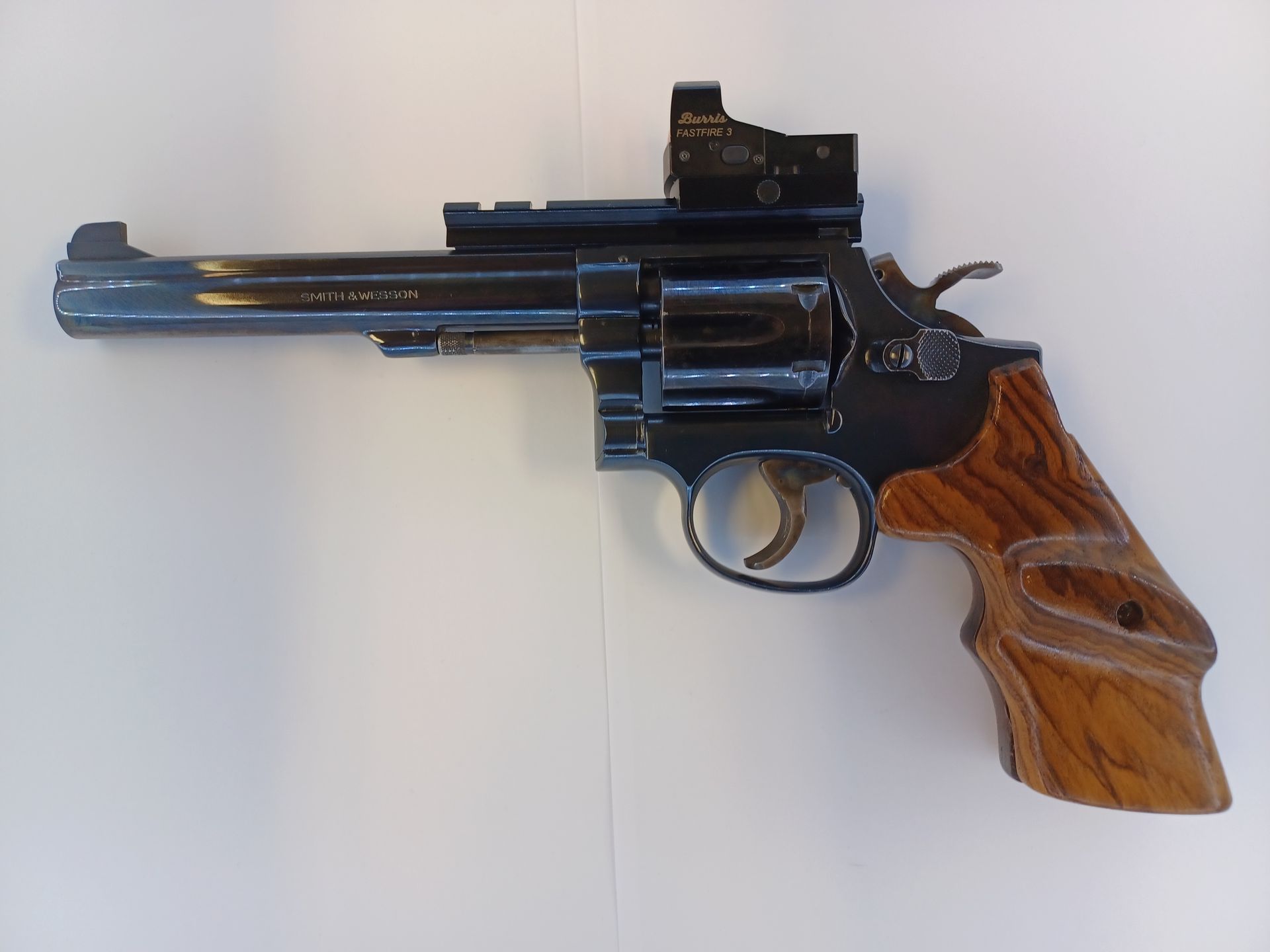 A black revolver with wood grip and a red dot sight, on a white surface.