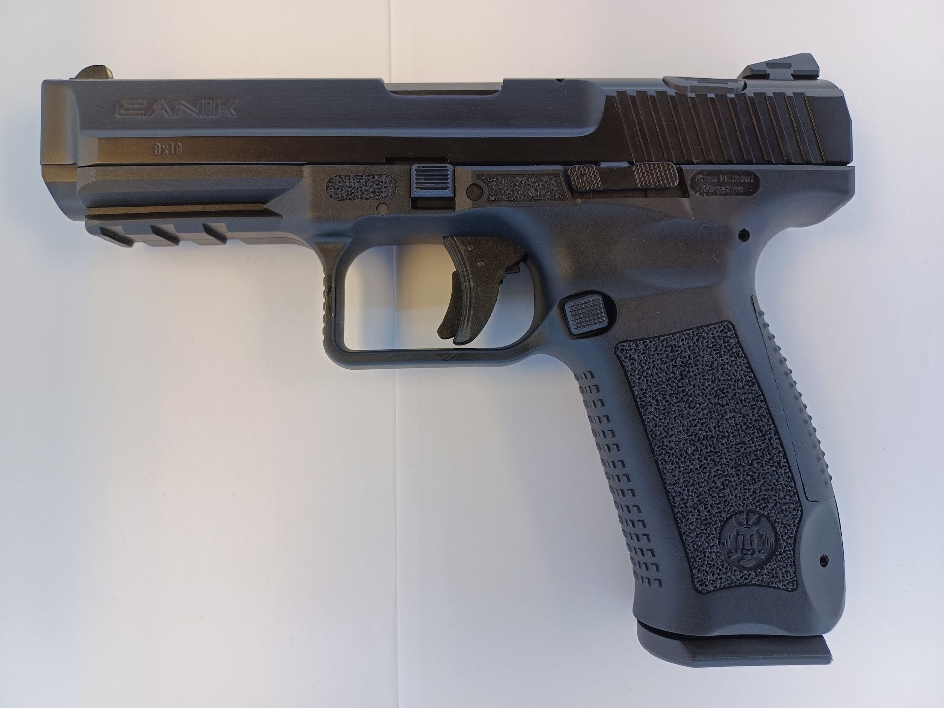 Black semi-automatic handgun, textured grip and slide, resting on a white surface.