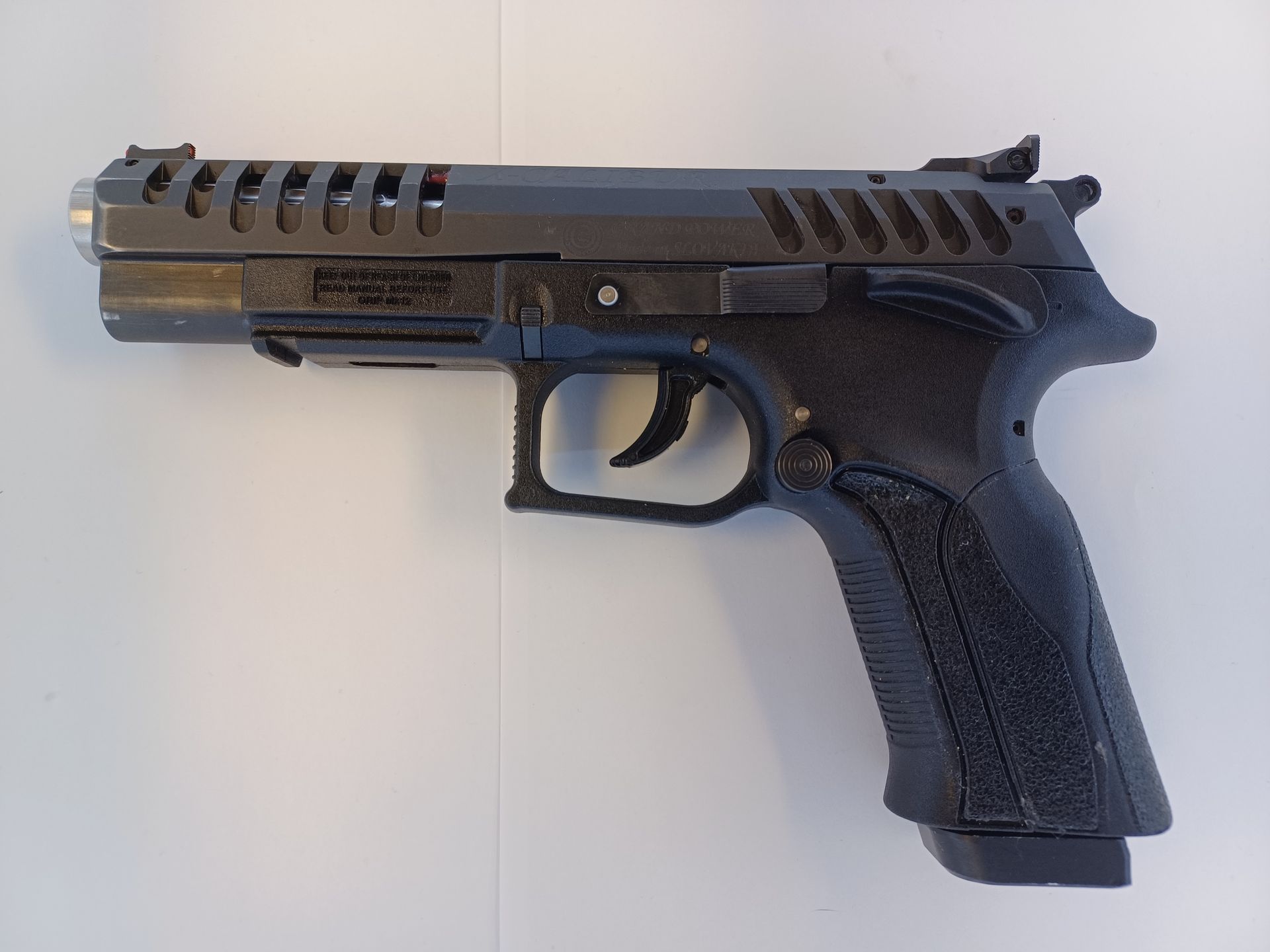 Black handgun on a white surface, seen from the side.
