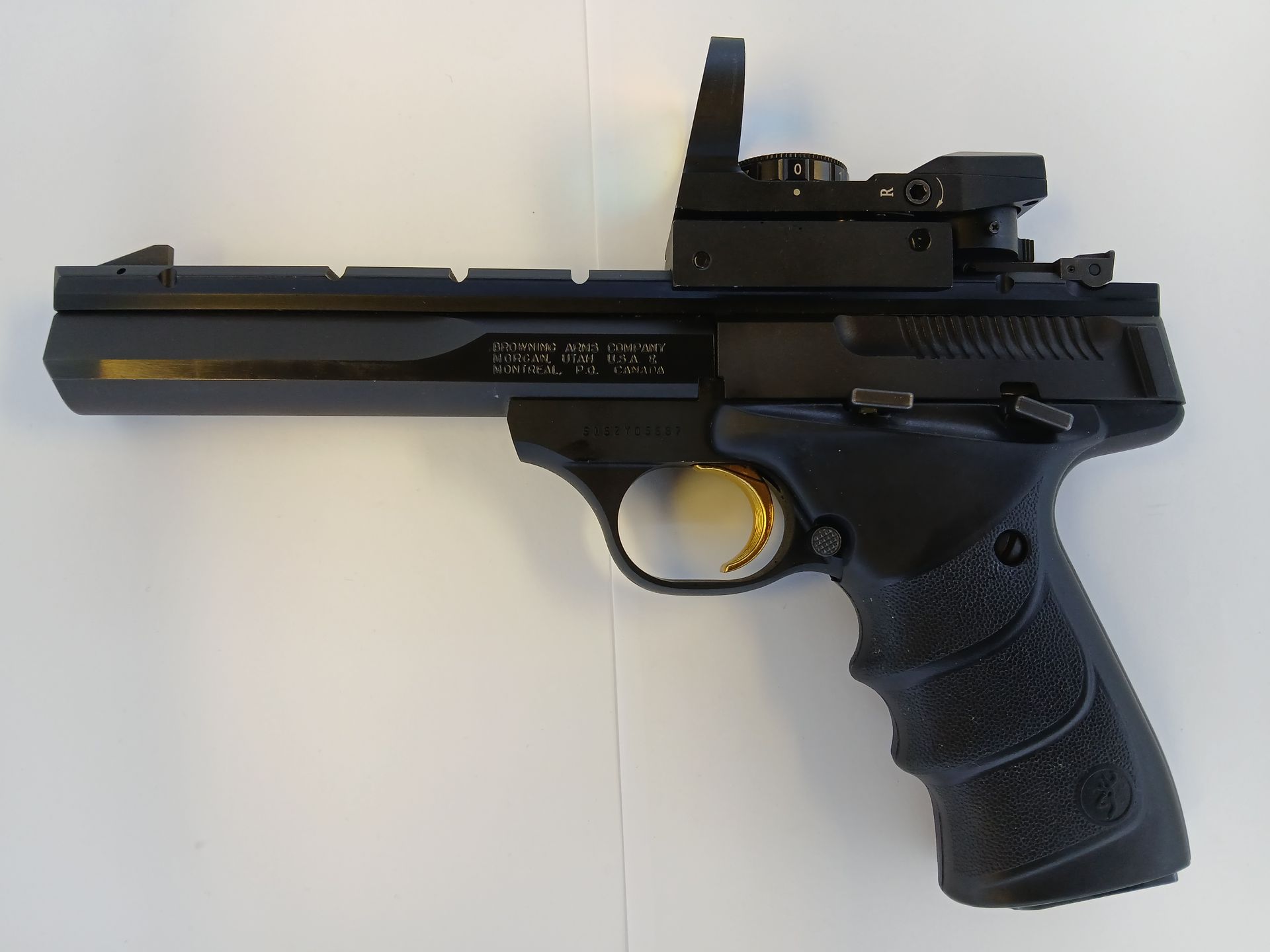 Black handgun with a red dot sight, resting on a white surface.
