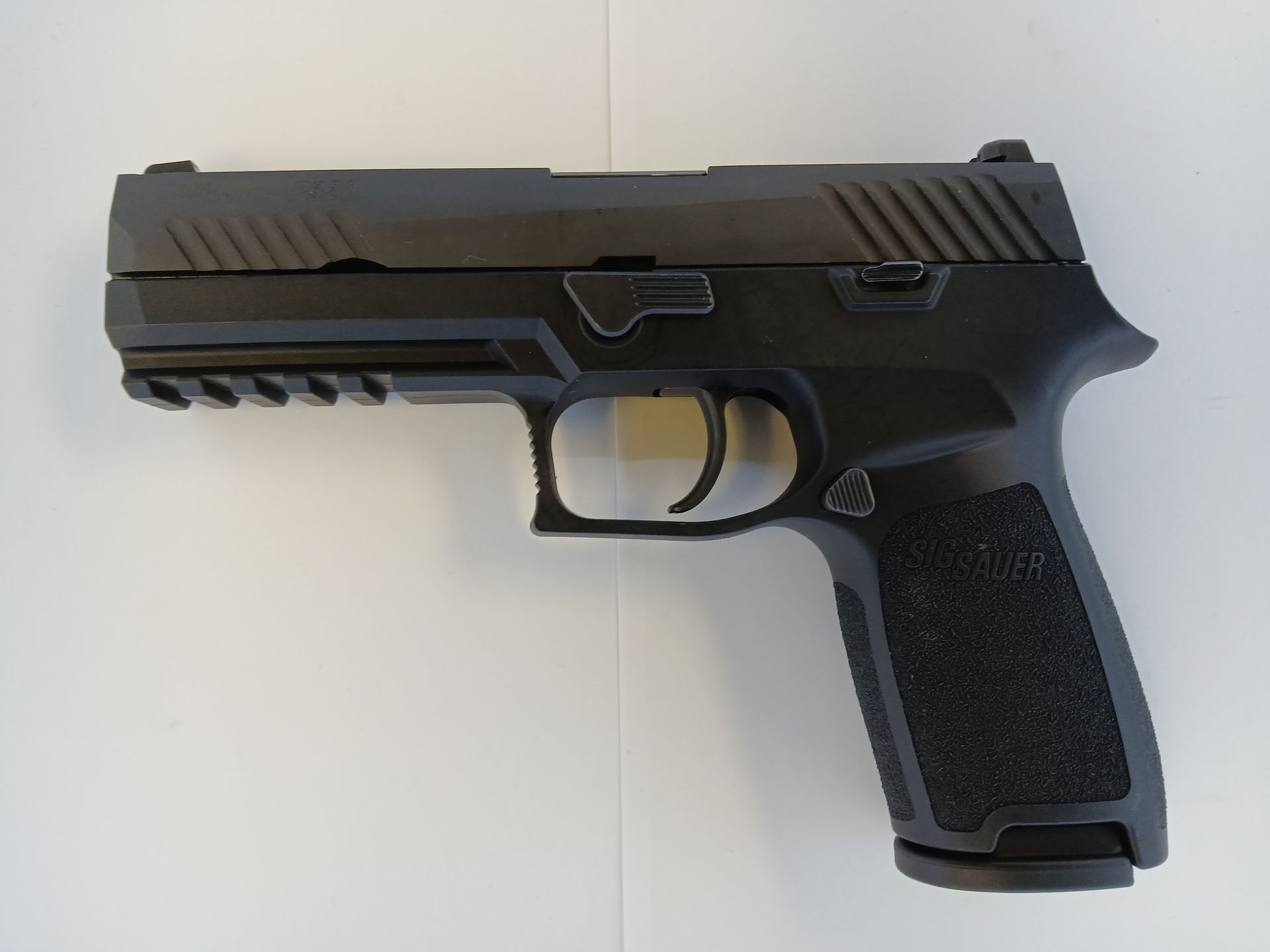 Black semi-automatic handgun on a white surface, angled right.