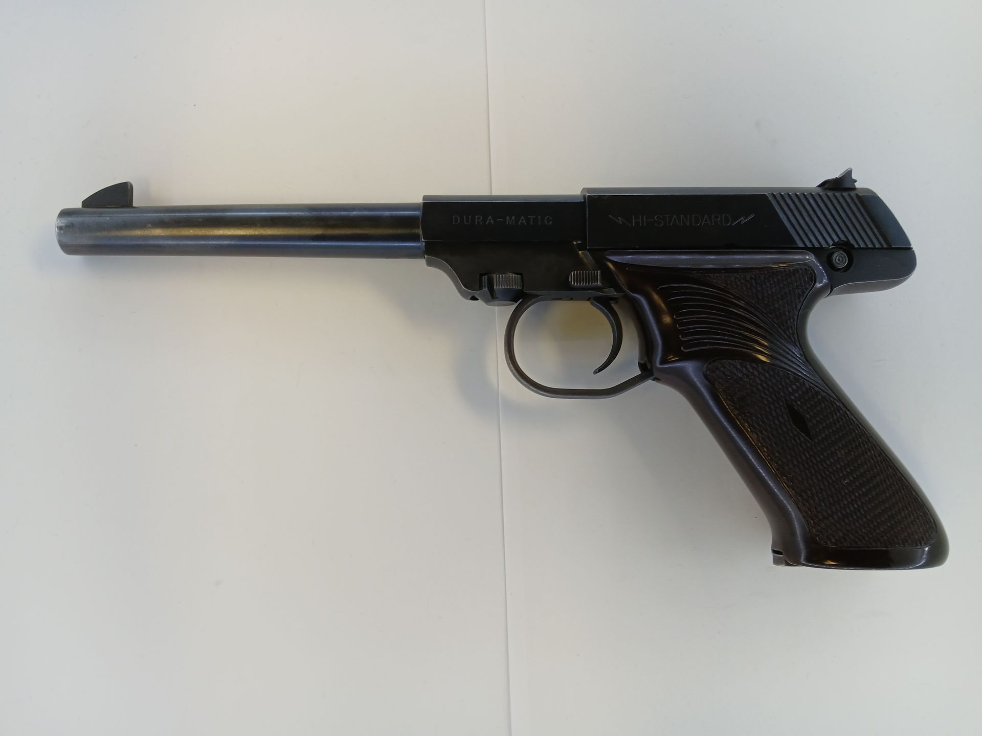 Black pistol on a white surface, with a long barrel and textured grip.