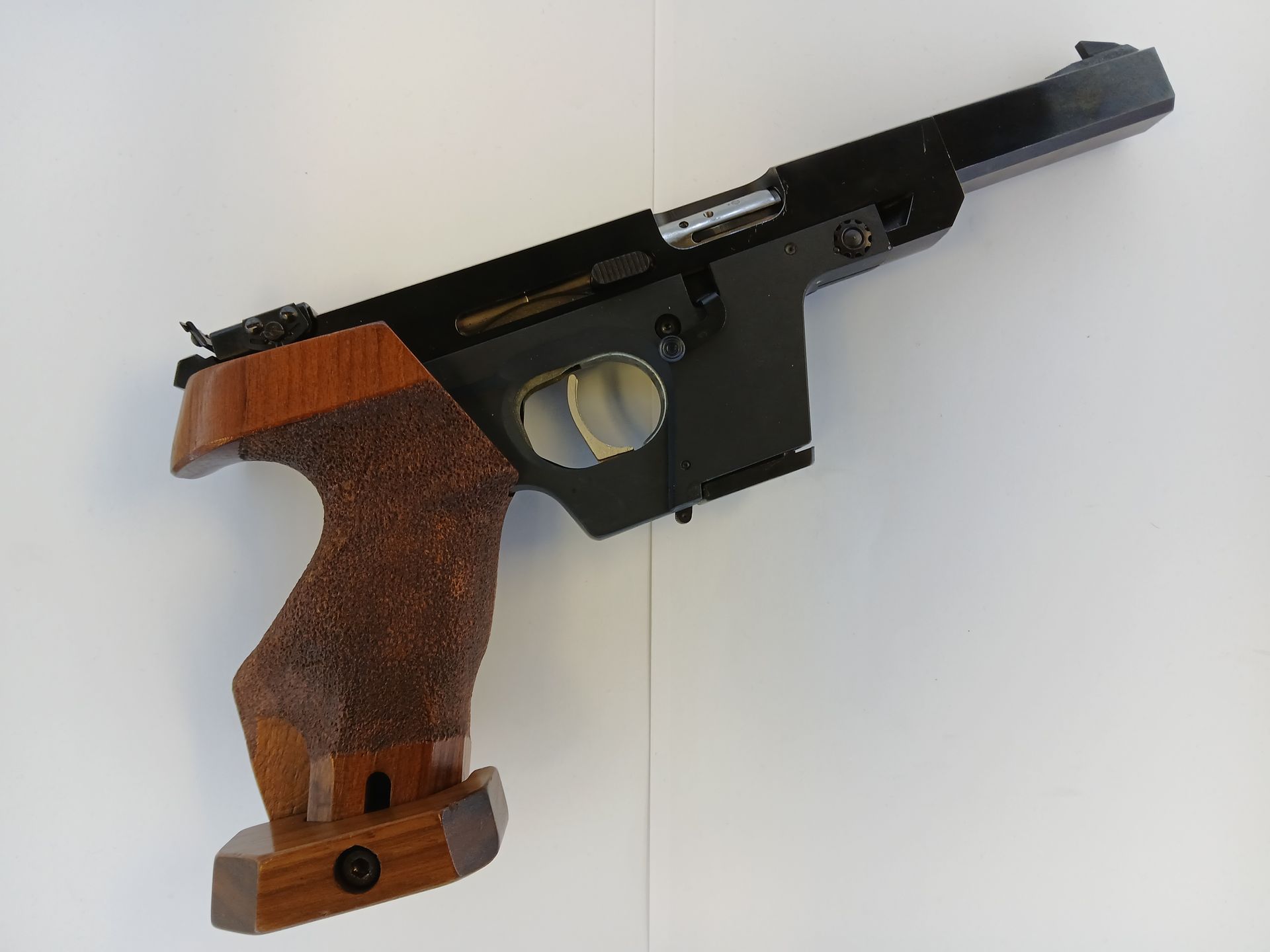 Target pistol with a wooden grip, brown and black, angled on a white surface.