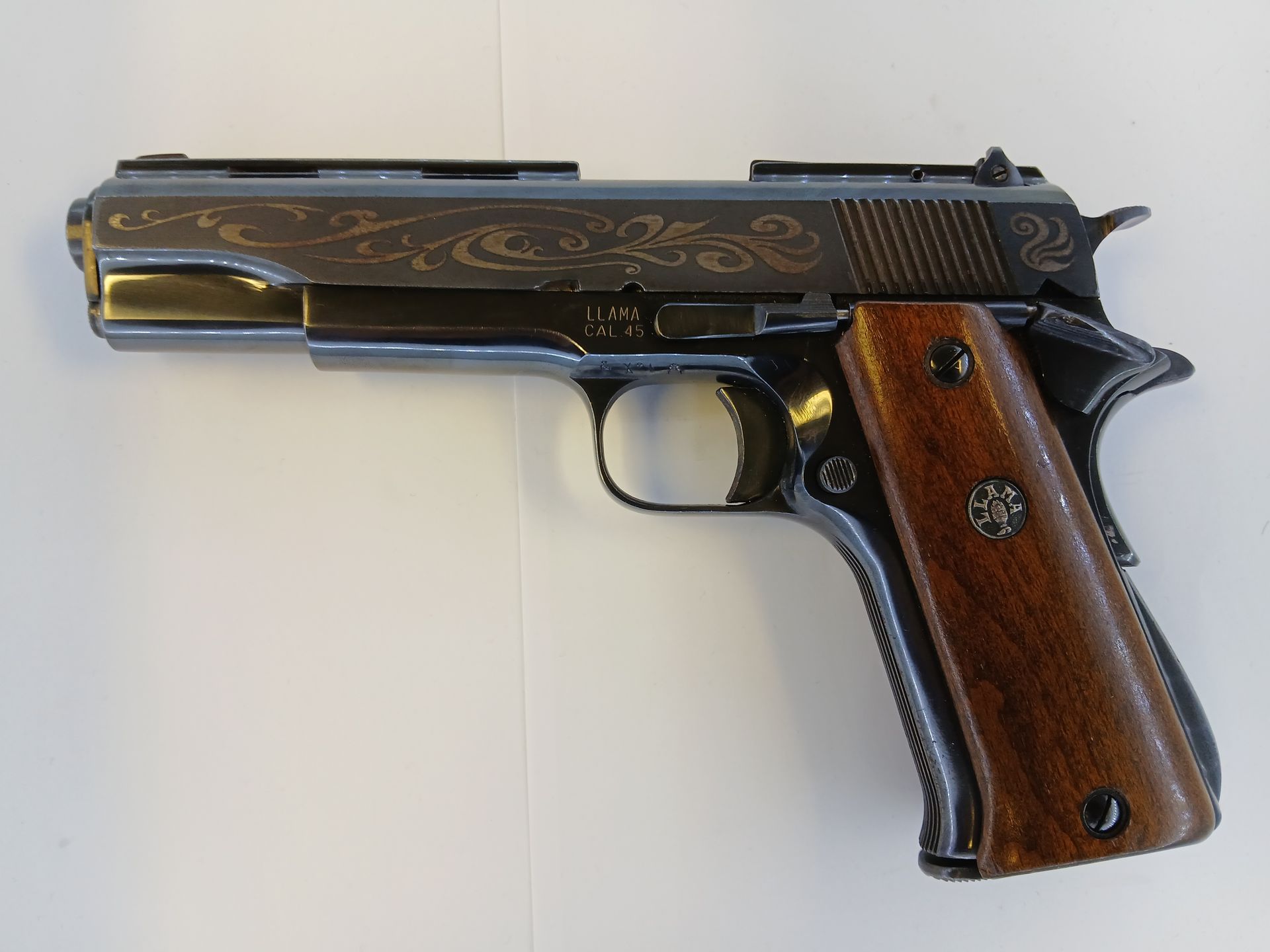 A black and silver engraved handgun with wooden grips, lying on a white surface.