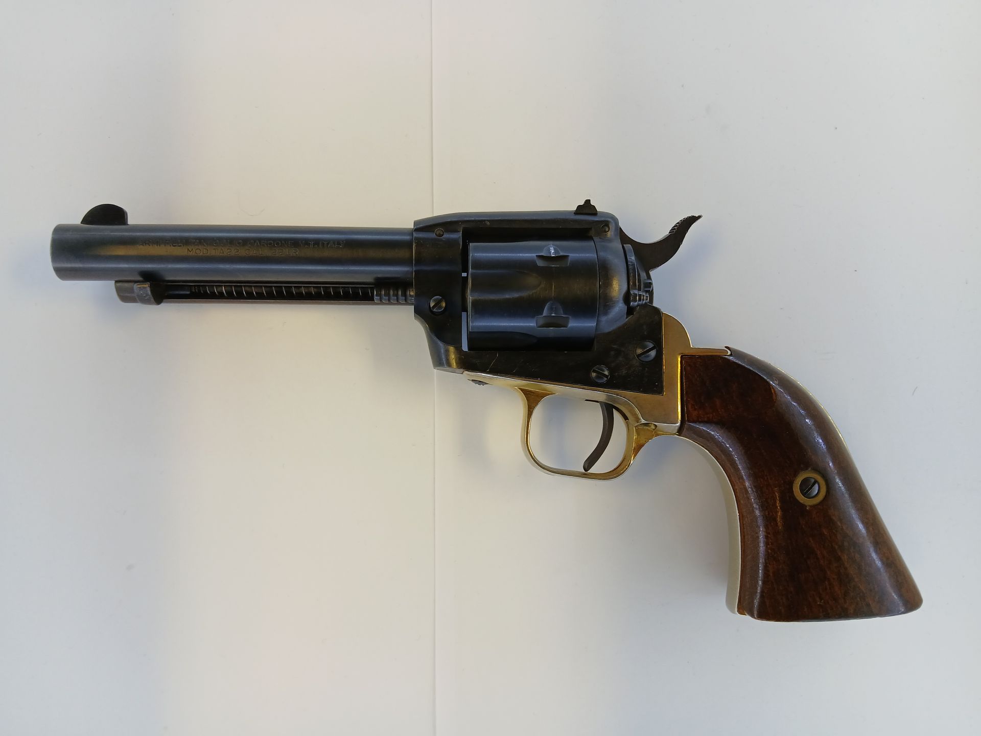 Black and gold revolver with wooden grip, lying on a white surface.