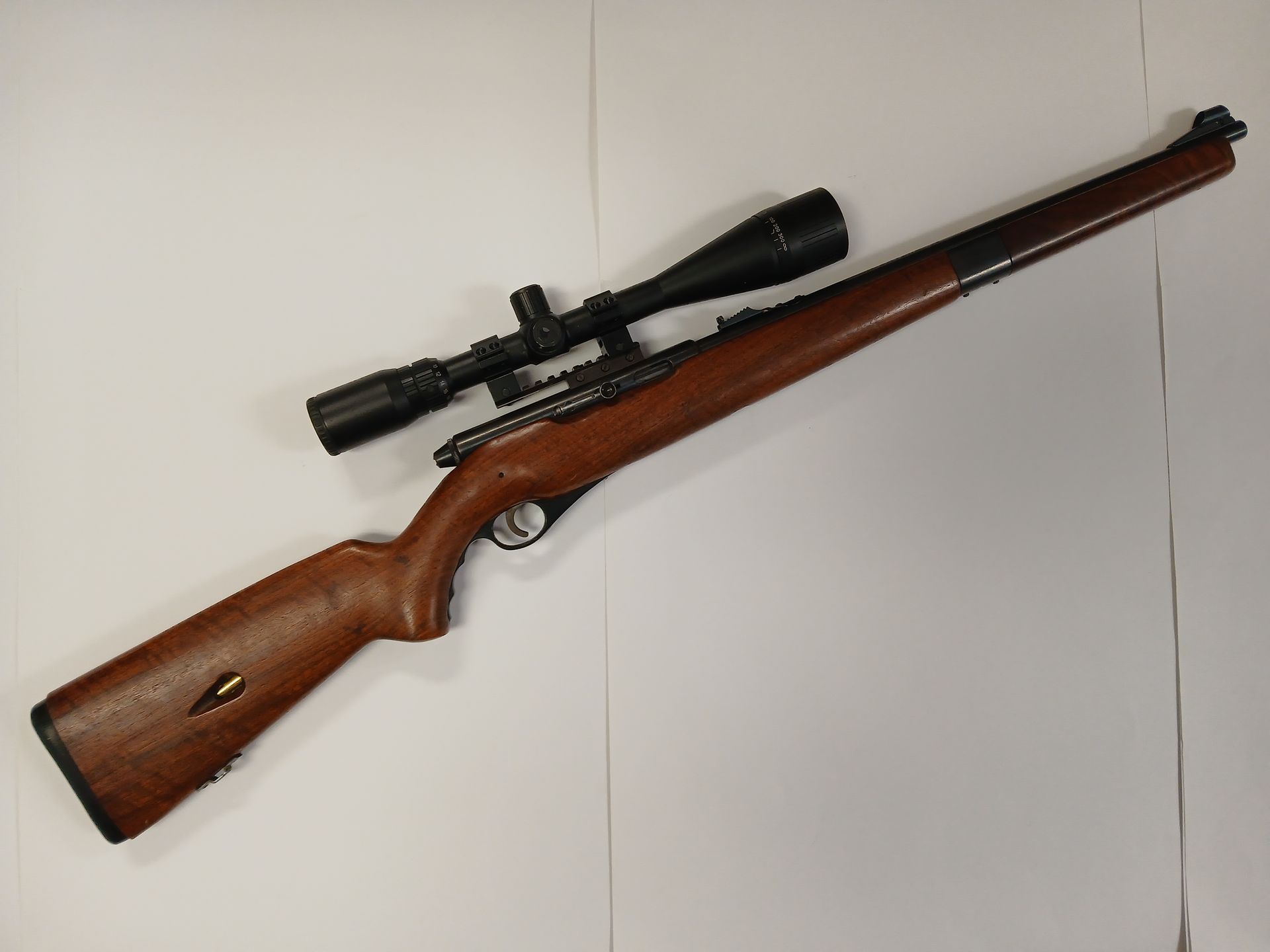 Brown rifle with a scope on a white surface.