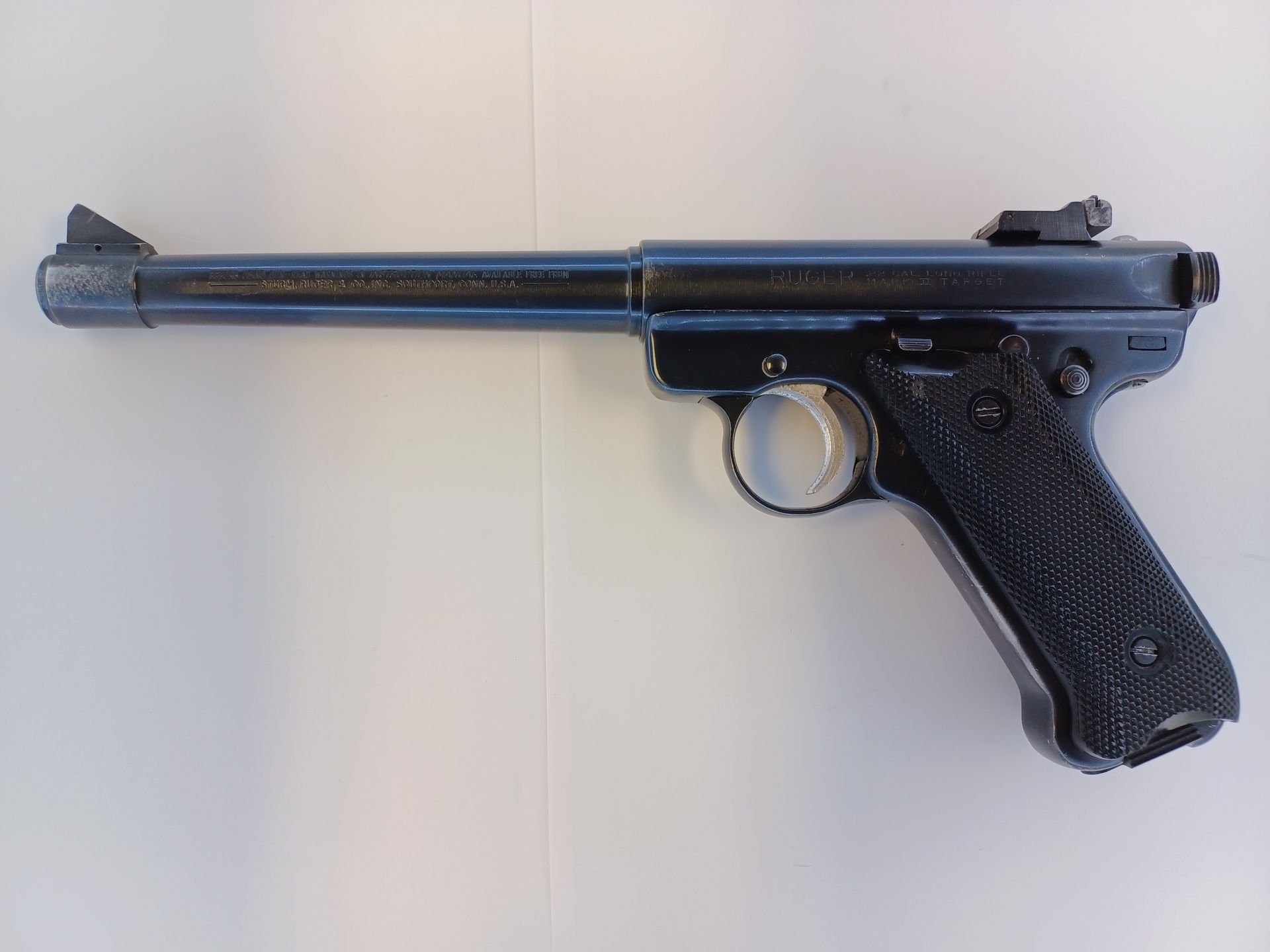 Black pistol with long barrel and textured grip, resting on a white surface.