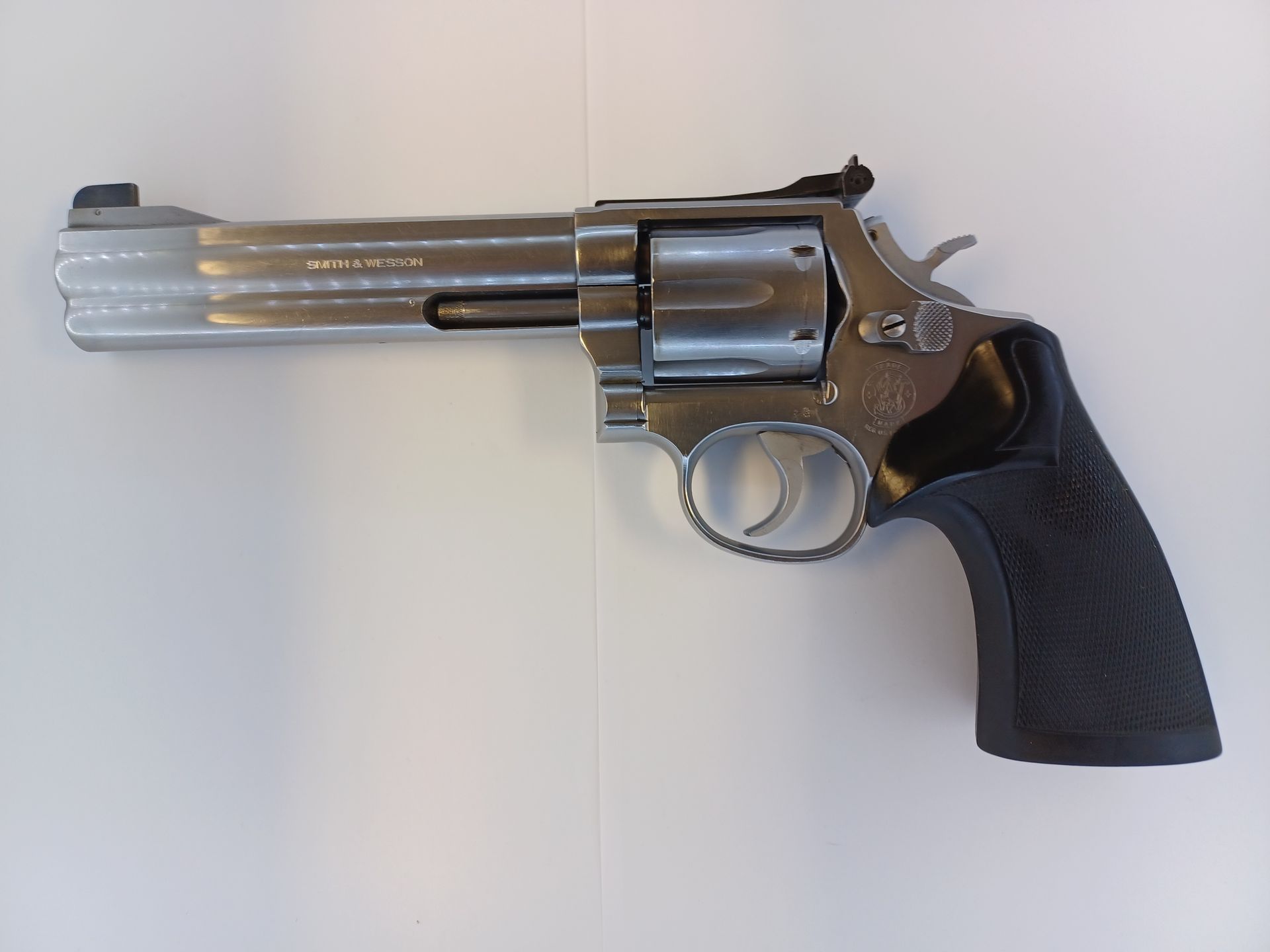 Silver revolver handgun with black grip, on a white surface.
