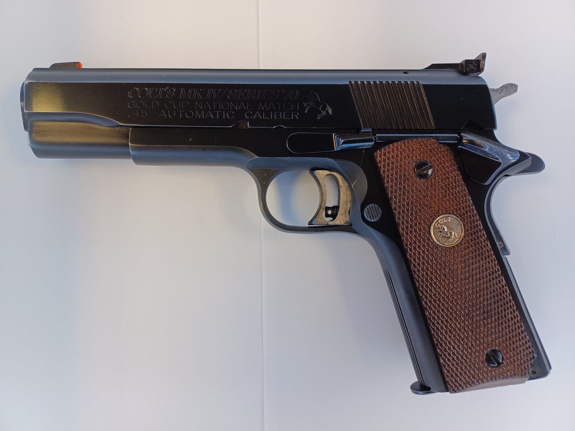 Black and brown handgun with wood grips. Silver trigger and red front sight.