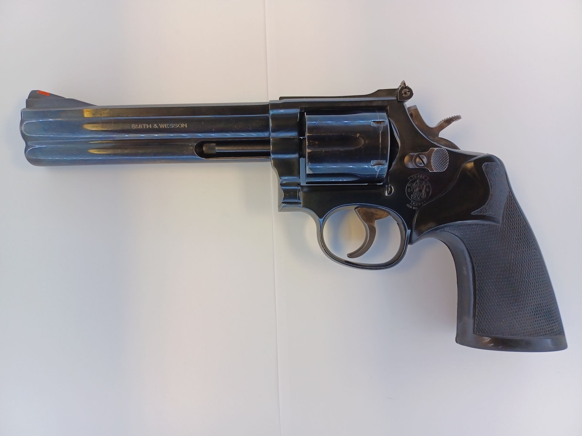Black revolver on a white surface, with a long barrel, visible cylinder, and textured grip.