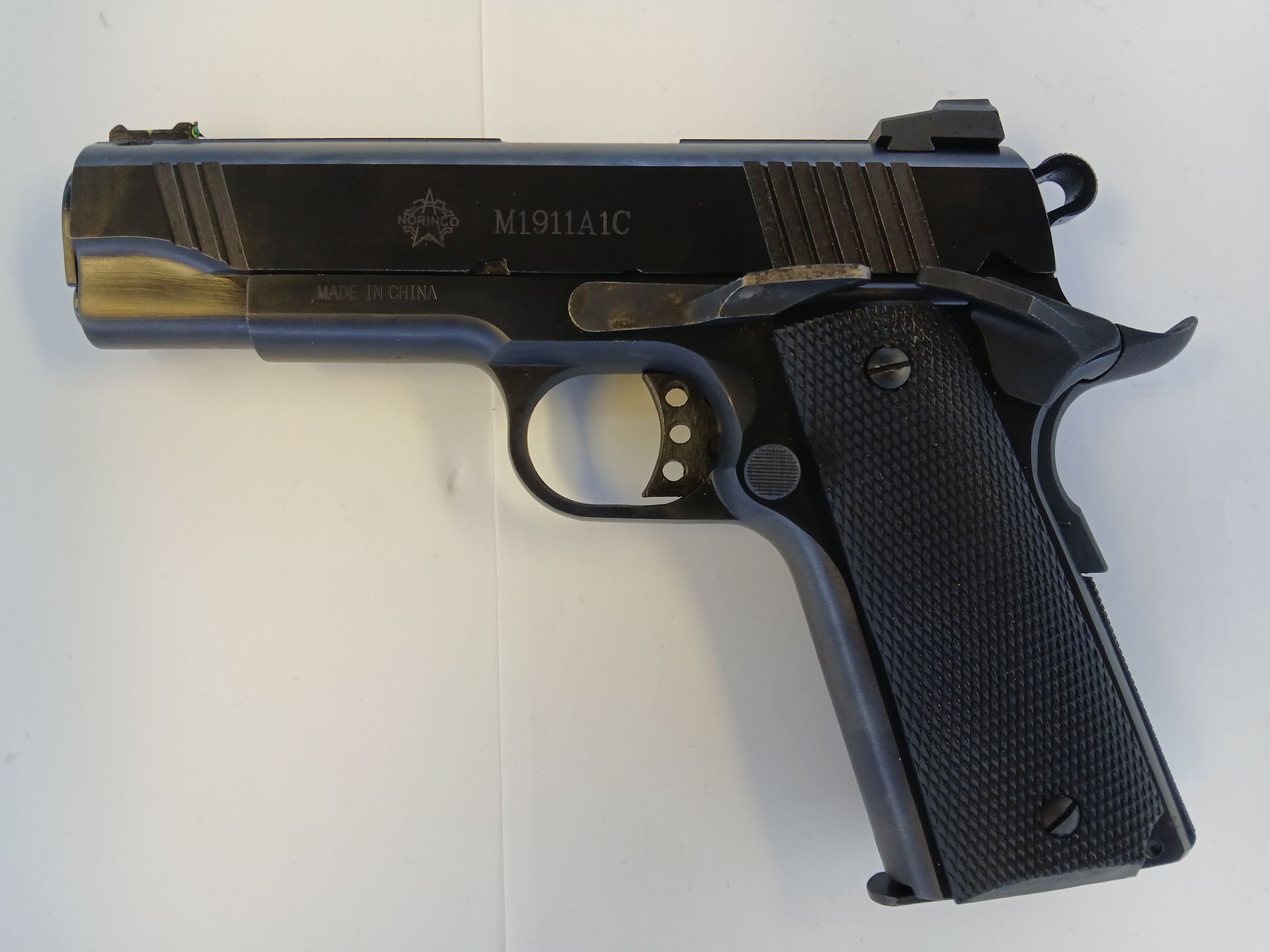 Black M1911A1 pistol with checkered grip, resting on a white surface.