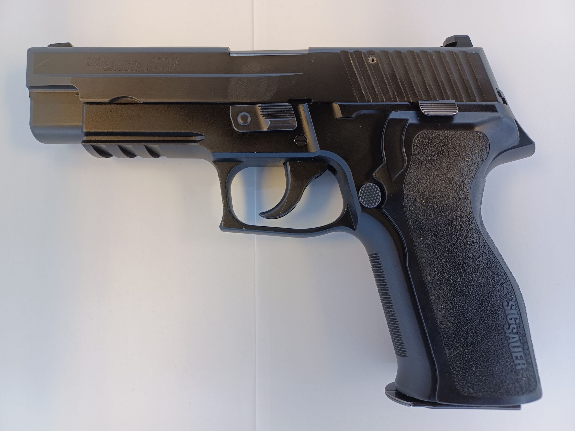 Black Sig Sauer P226 pistol on a white surface, angled view, showing grip and slide details.