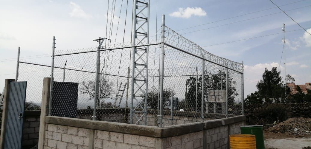 Una valla de alambre rodea un edificio con una torre al fondo.
