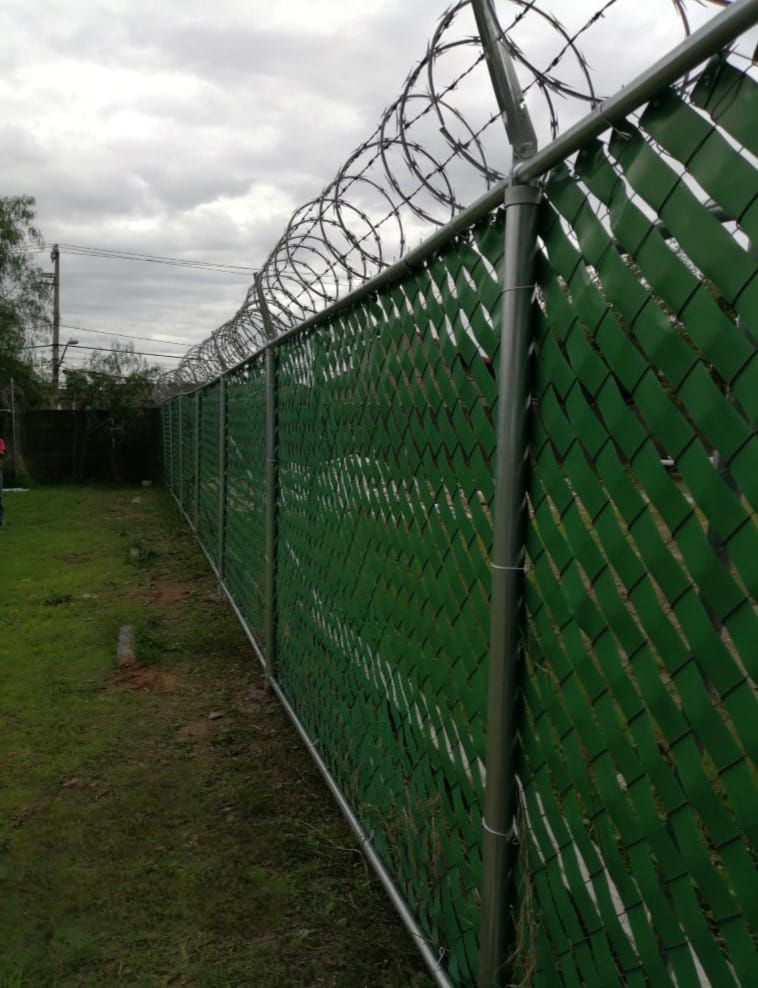 Una valla de alambre verde con alambre de púas en la parte superior