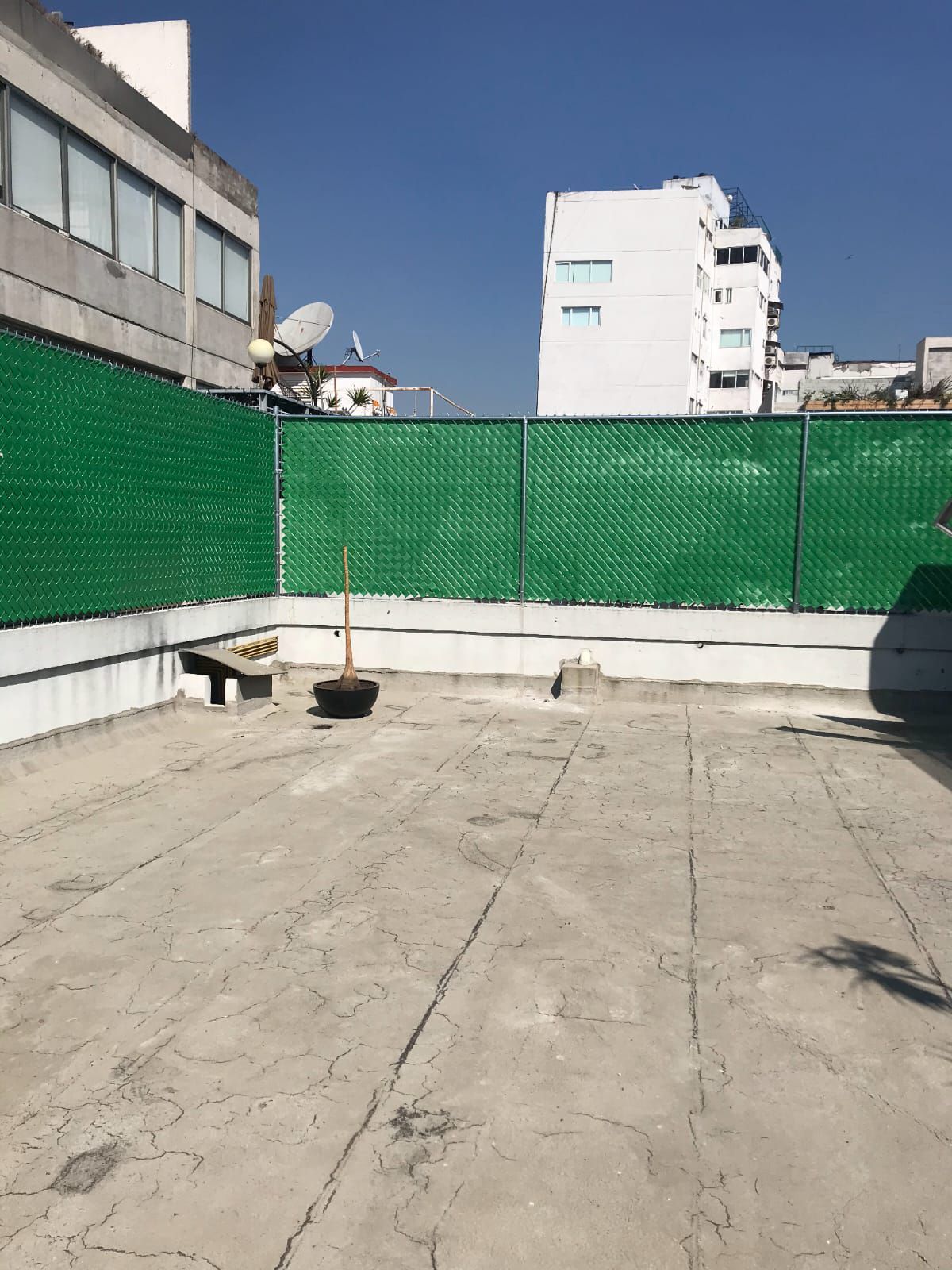 Un patio de hormigón con una valla verde y un edificio al fondo.