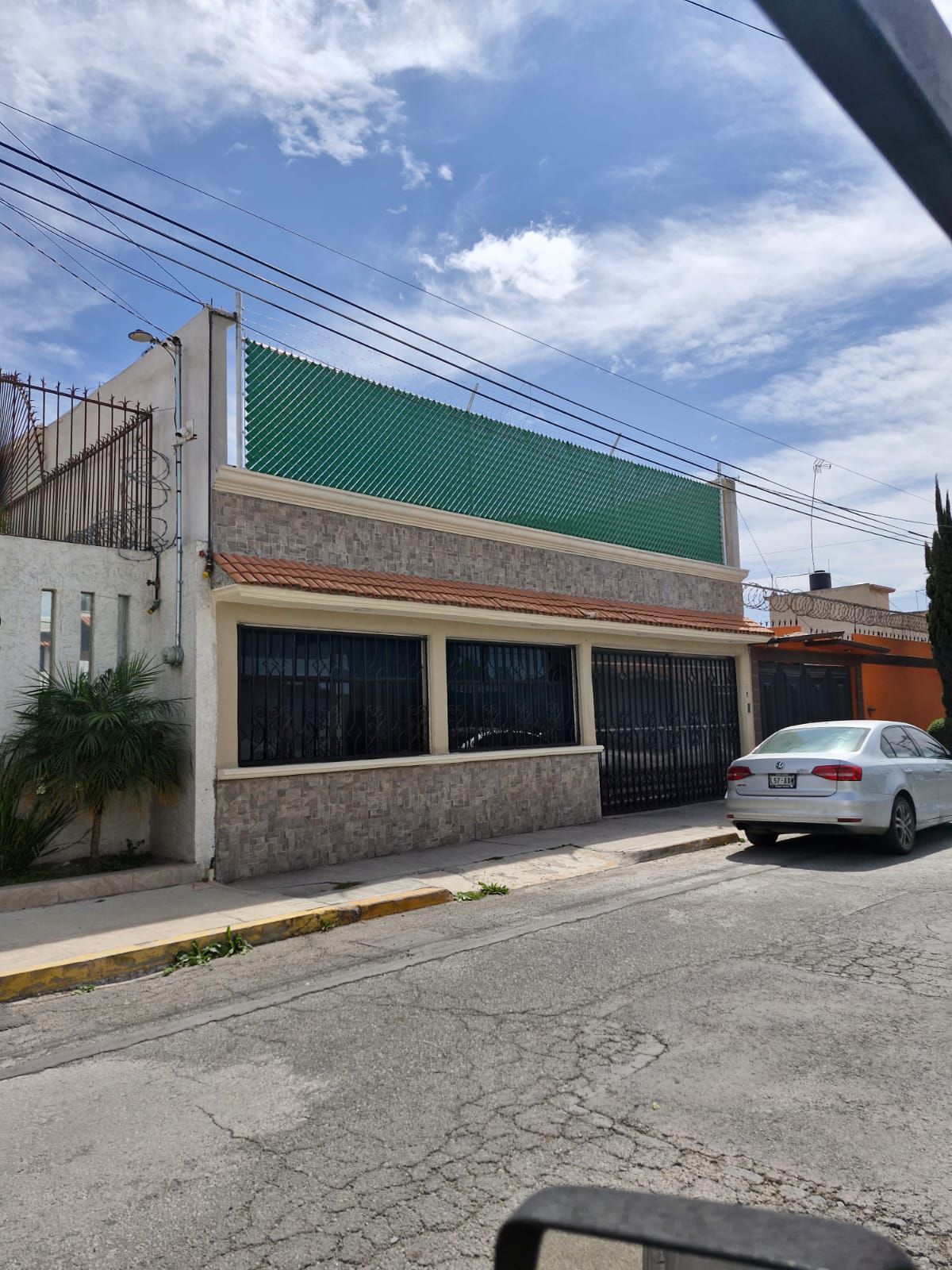 Un coche blanco está aparcado delante de una casa con una valla verde.