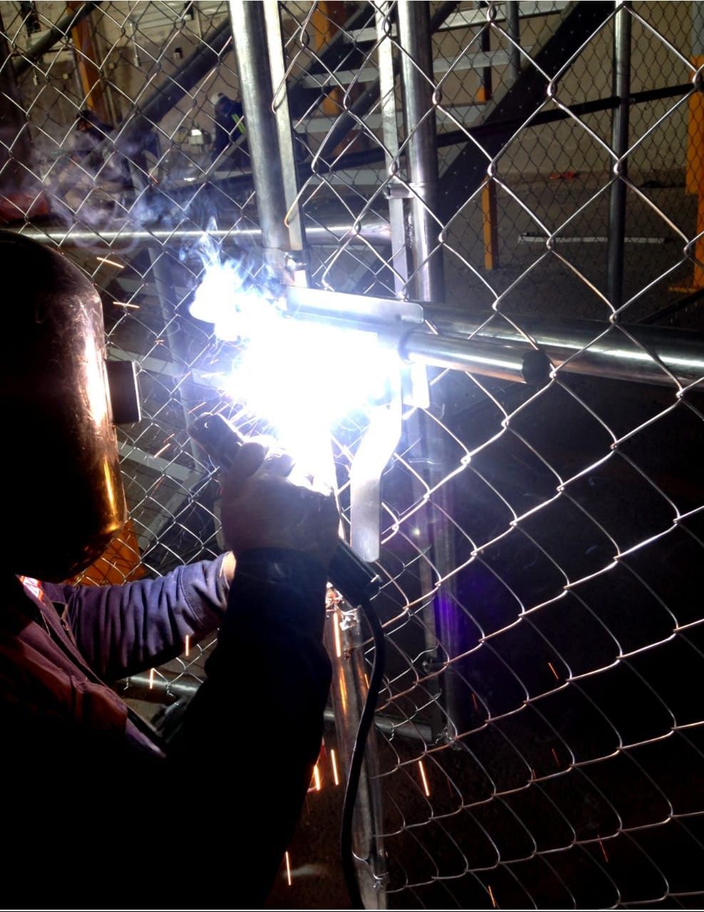 Un hombre está soldando una cerca de alambre en una habitación oscura.