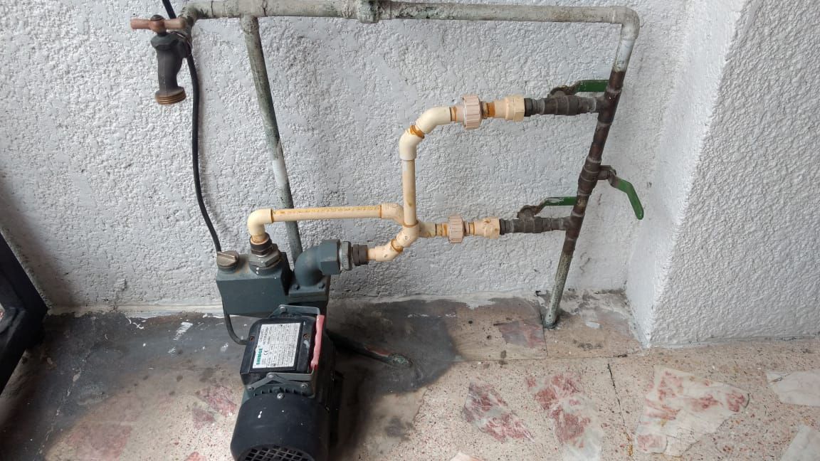 Una bomba de agua está colocada junto a una pared con tuberías conectadas a ella.