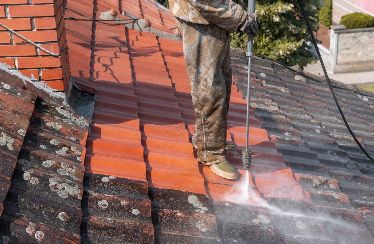 A man is cleaning a tiled roof with a high pressure washer.