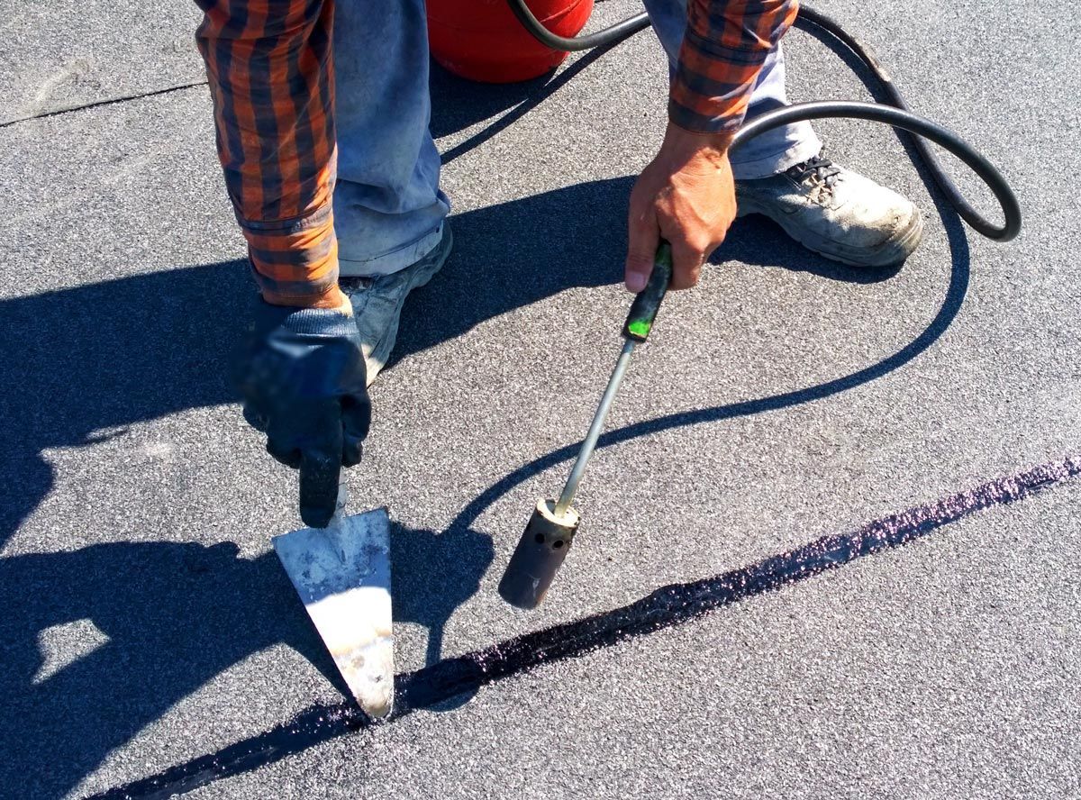 A man is using a spatula and a torch on a concrete surface