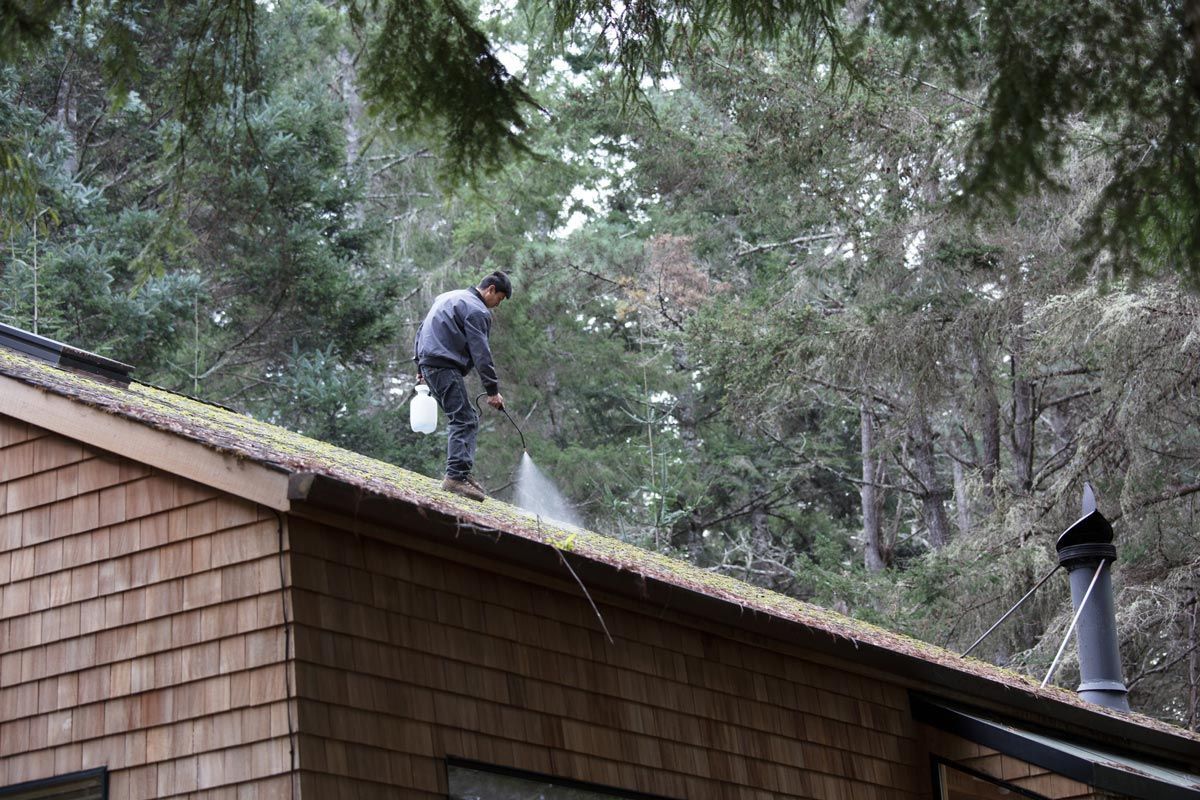 A man is spraying water on the roof of a house.