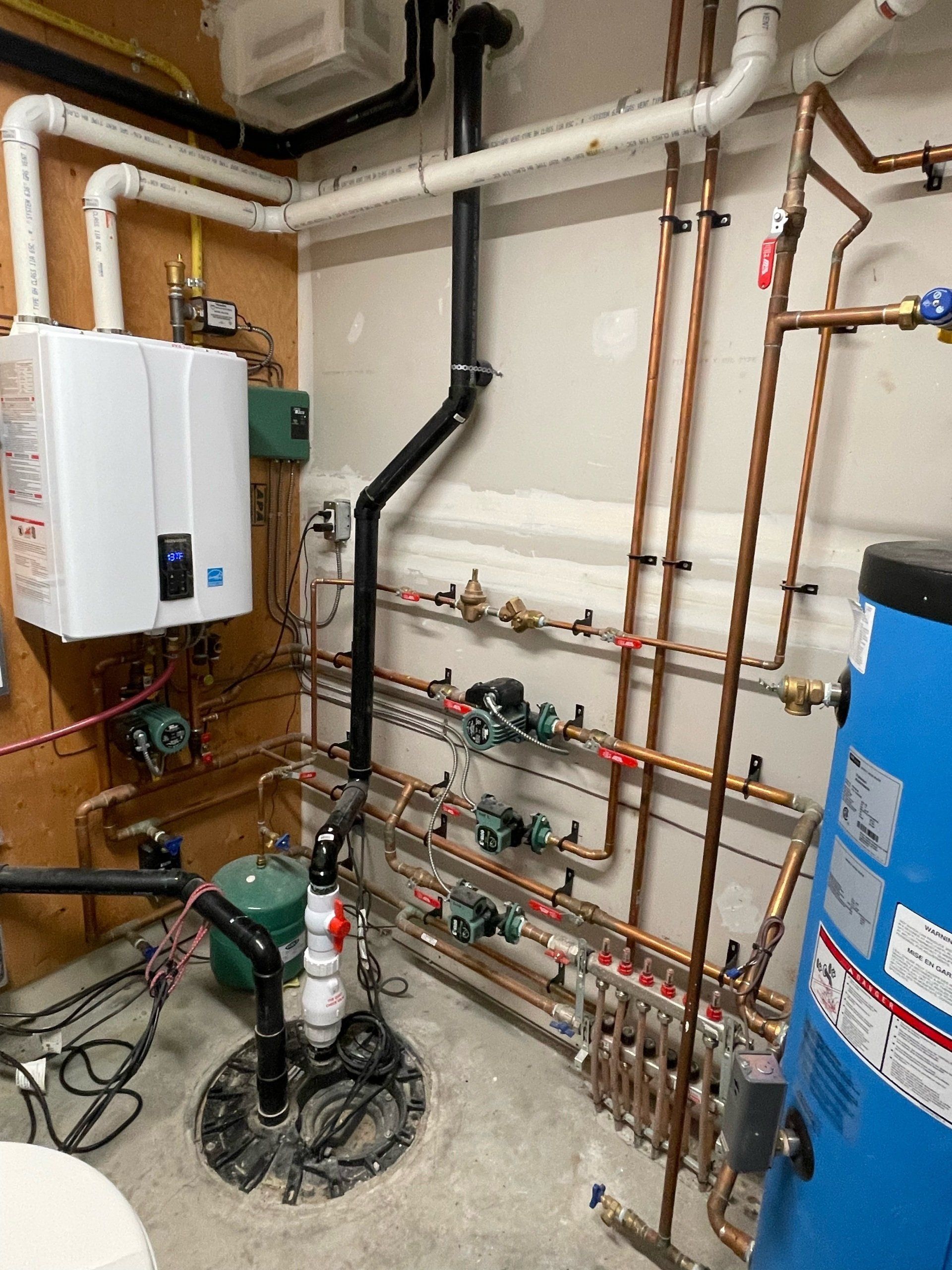 A room with a lot of pipes and a blue water heater.
